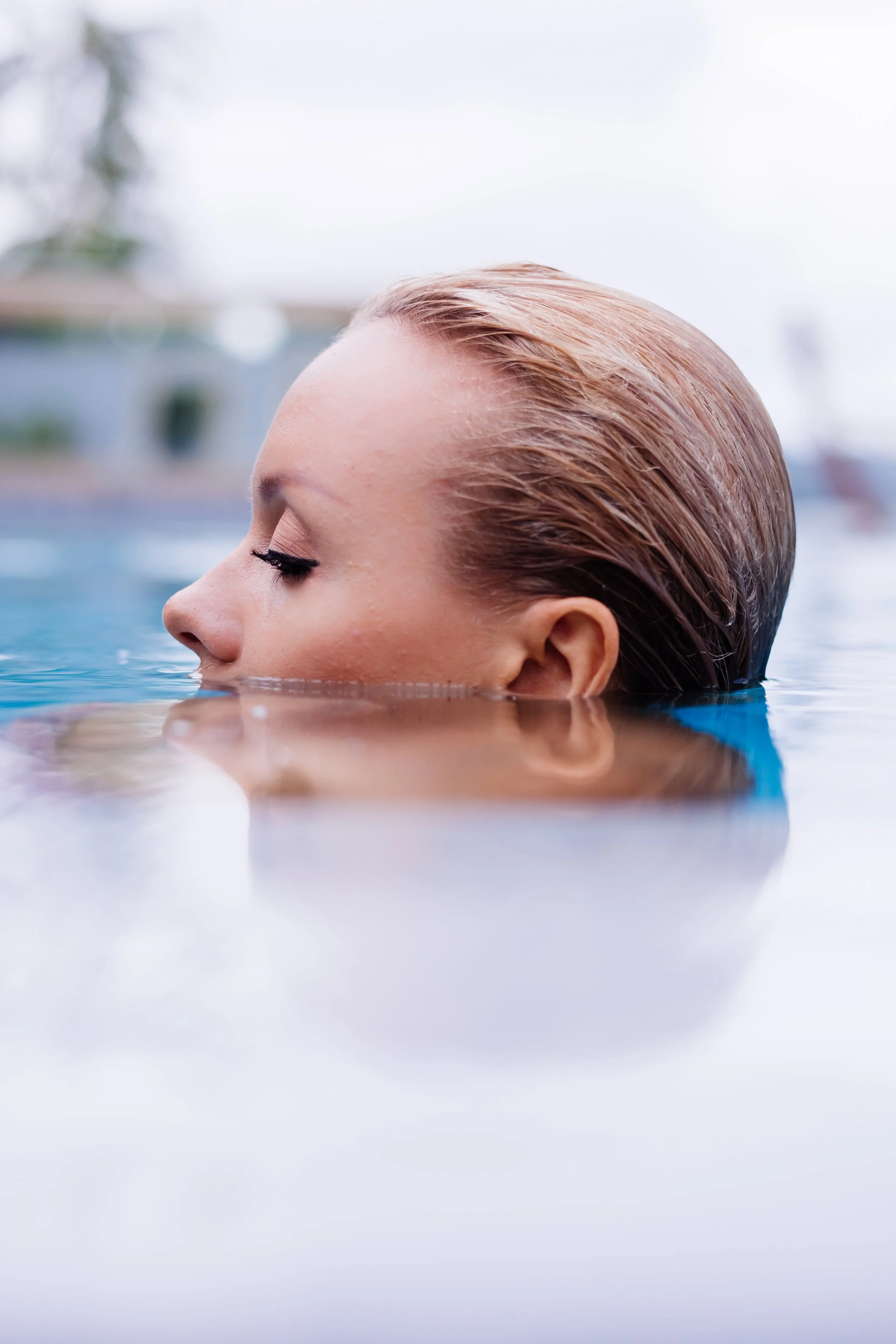 Close-up of a woman with slicked-back blonde hair submerged in water, with her eyes closed and face relaxed.