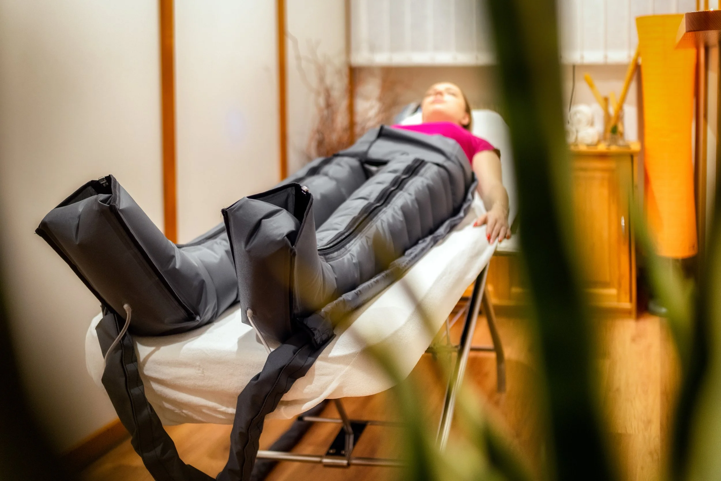 A woman lying on a treatment table wearing compression boots on her legs