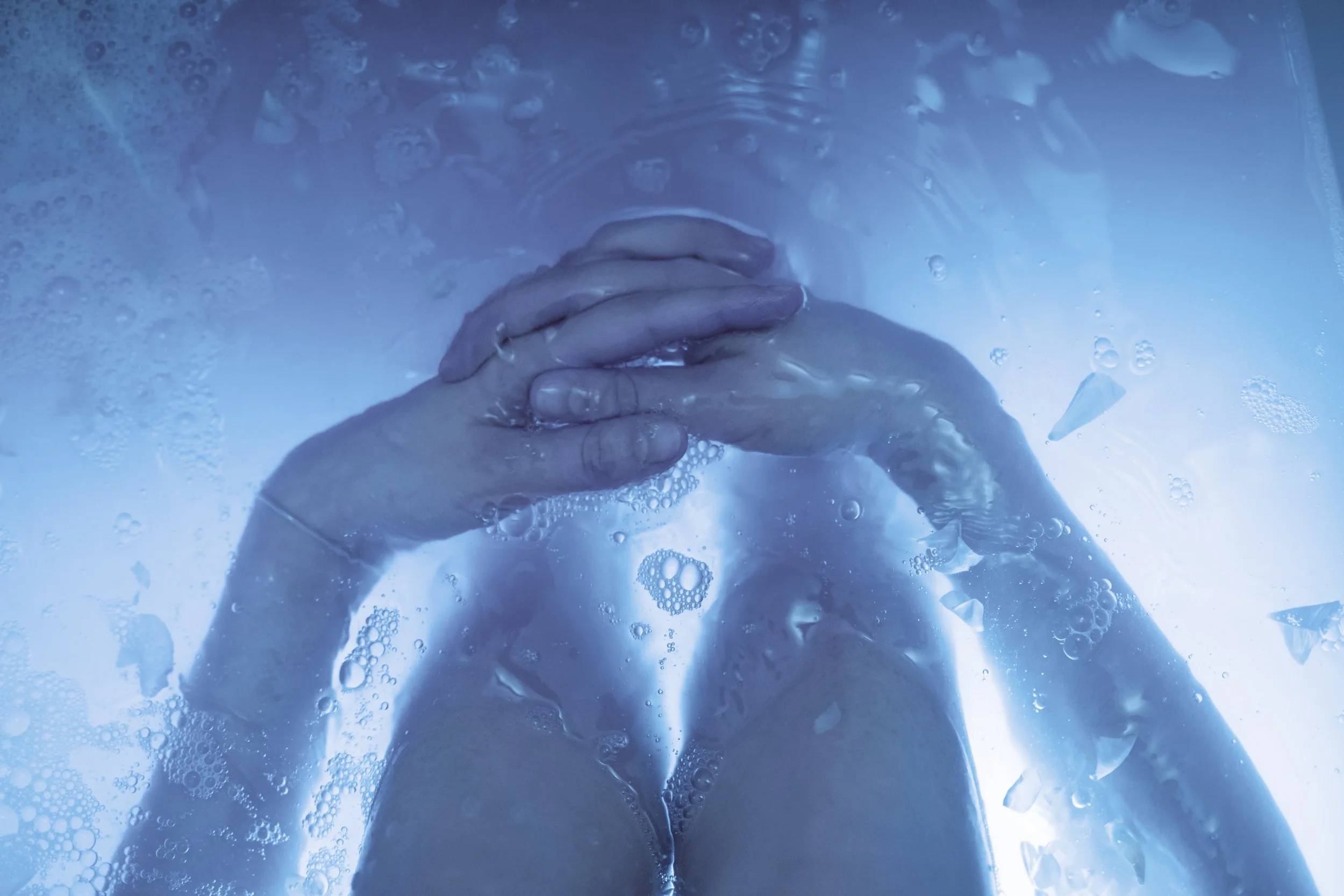 Hands clasped together in a cold plunge pool, illuminated by soft blue lighting.