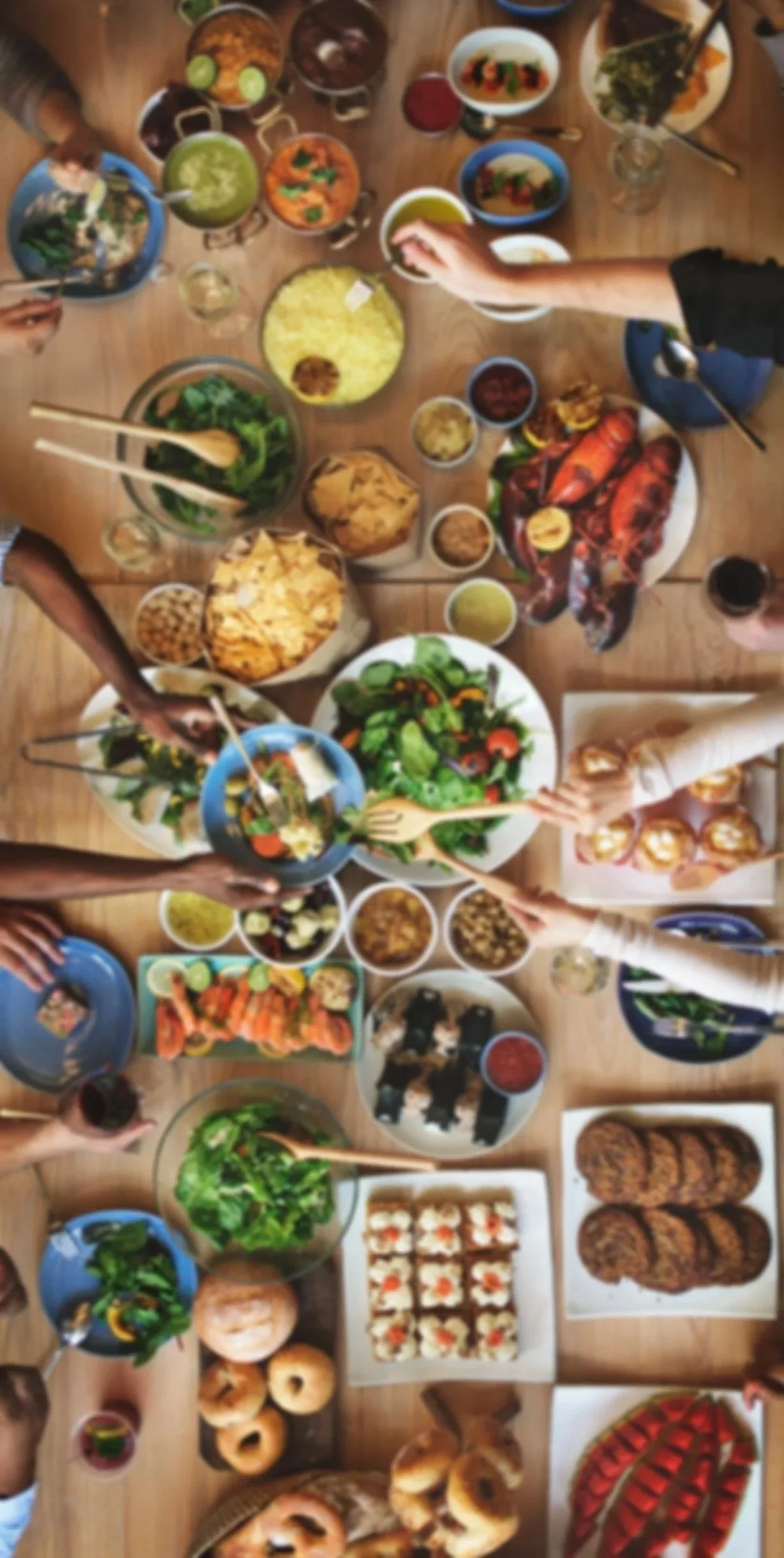 Top-down view of a table filled with various foods for a gathering, including salads, sushi, baked goods, desserts, and drinks.