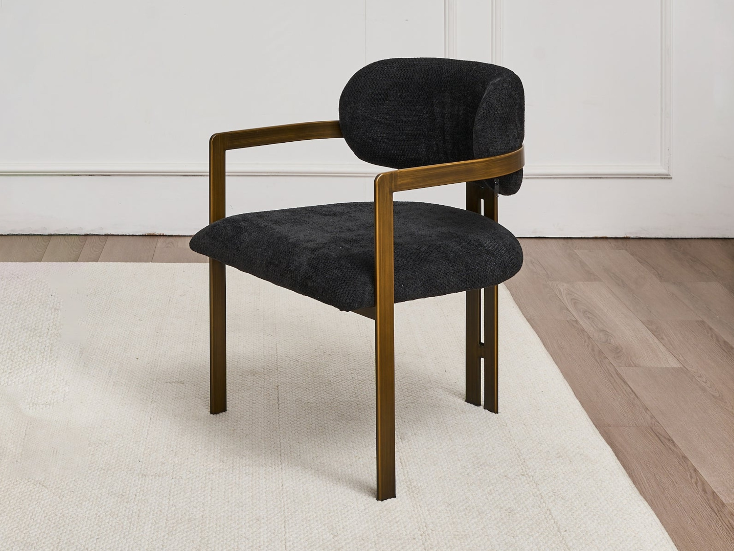 A black upholstered chair with wooden armrests and legs, placed on a light-colored carpet against a white wall with molding.
