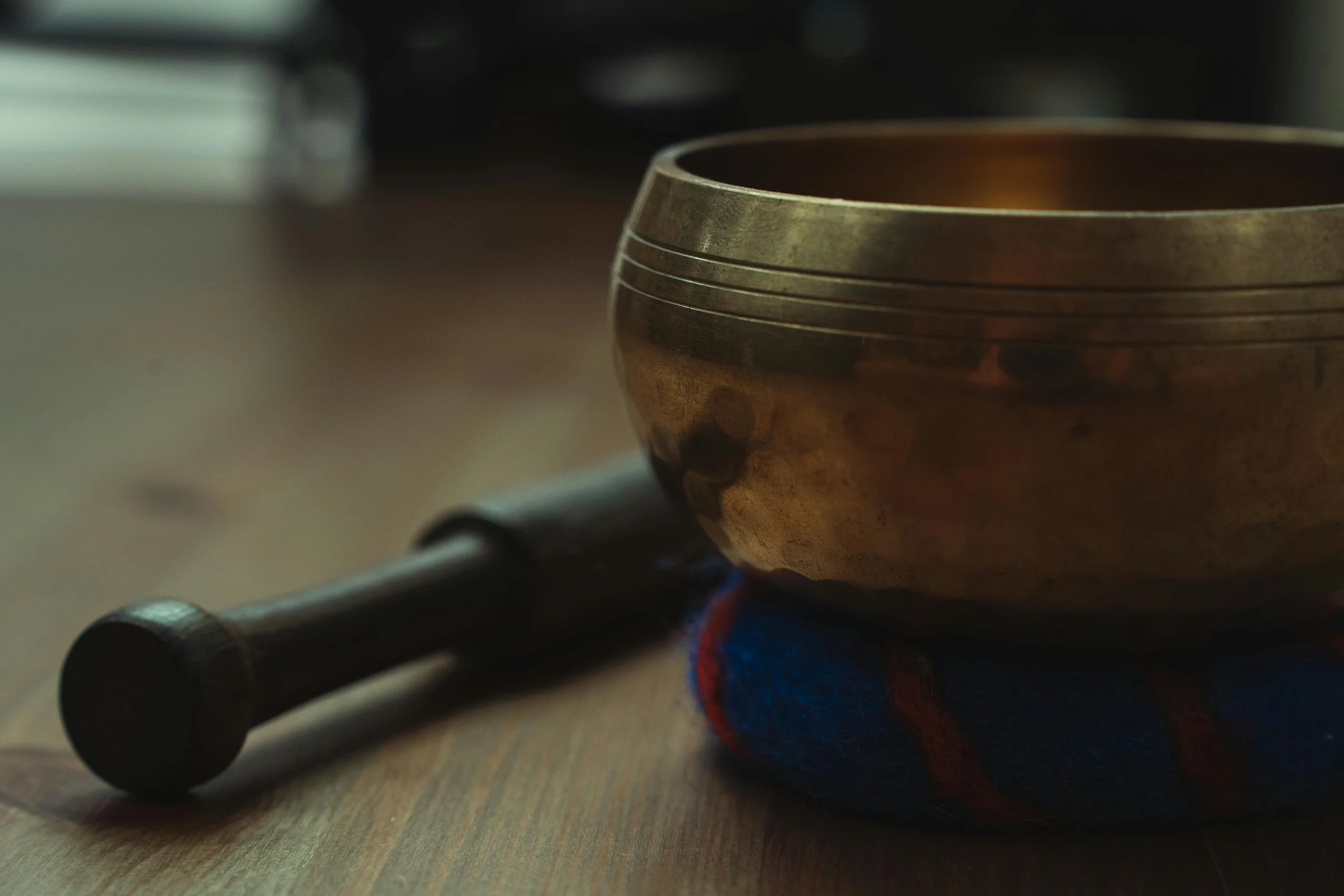 A handcrafted singing bowl with a wooden mallet resting beside it on a wooden surface.