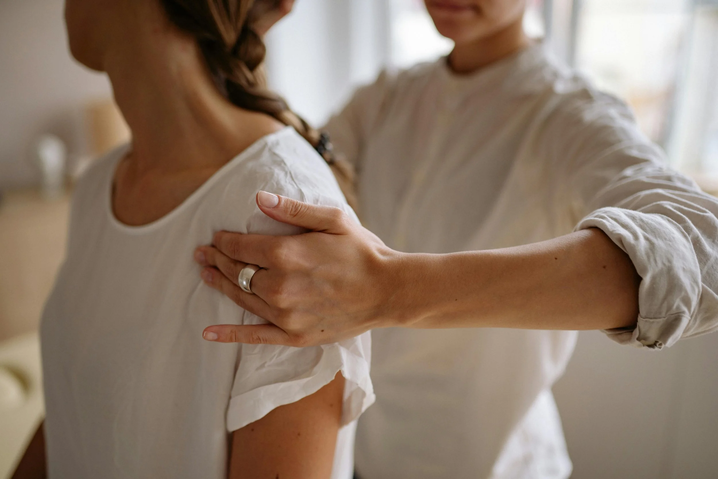 A person receiving a shoulder massage from another person, with both wearing white shirts indoors.
