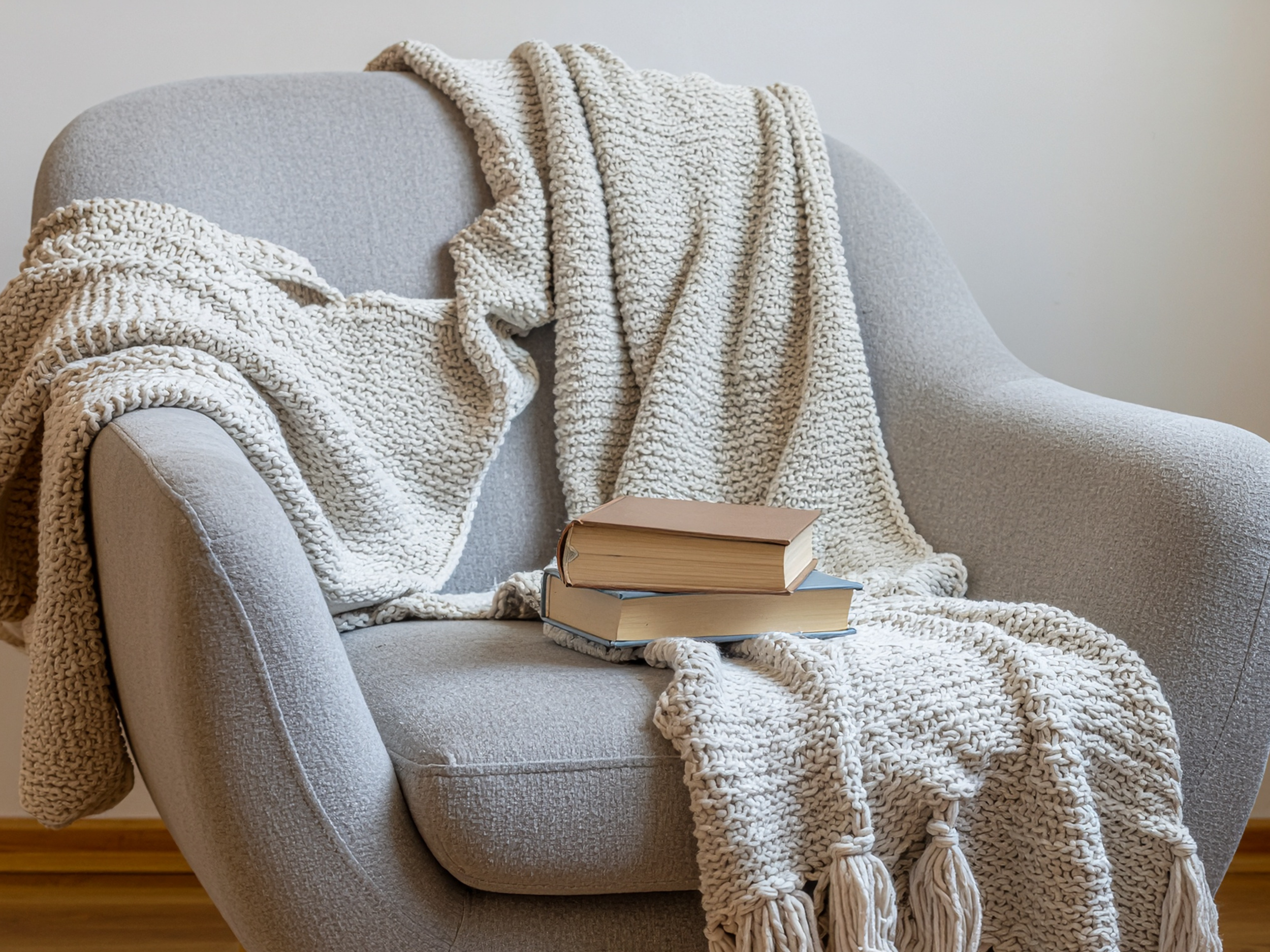 A gray armchair with a textured cream blanket draped over it, and two hardcover books stacked on the seat.