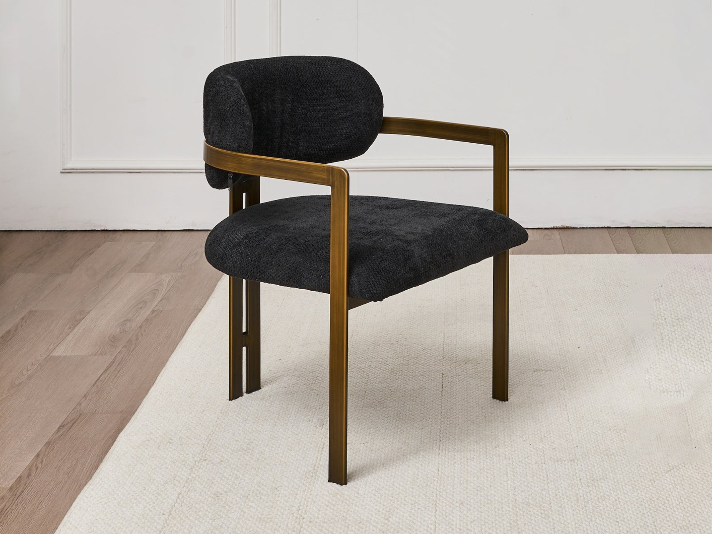 A modern black and gold armchair with a cushioned back and seat, placed on a light-colored rug in a room with white walls and hardwood flooring.