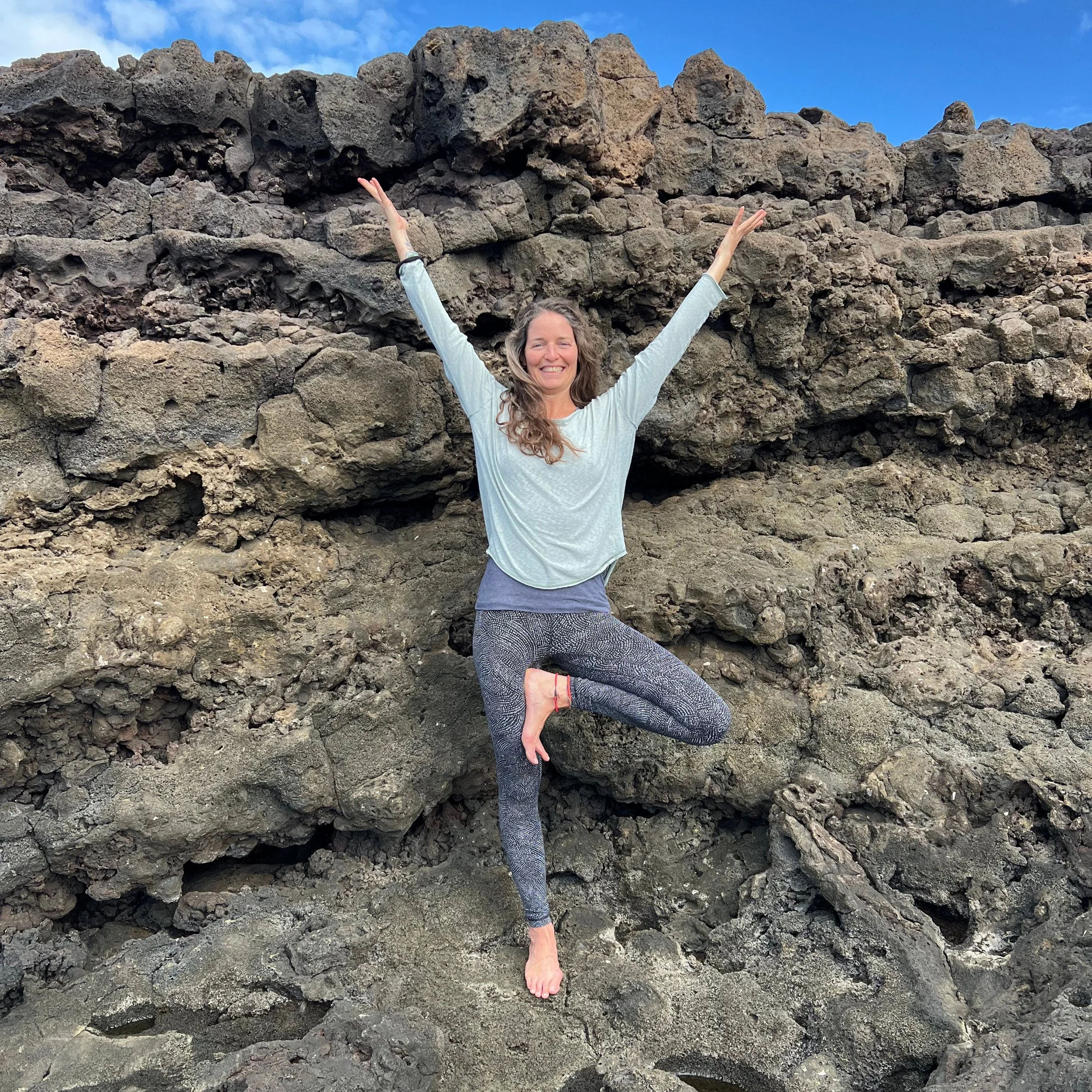 Una donna sorridente che fa yoga in posizione dell'albero su una roccia vulcanica
