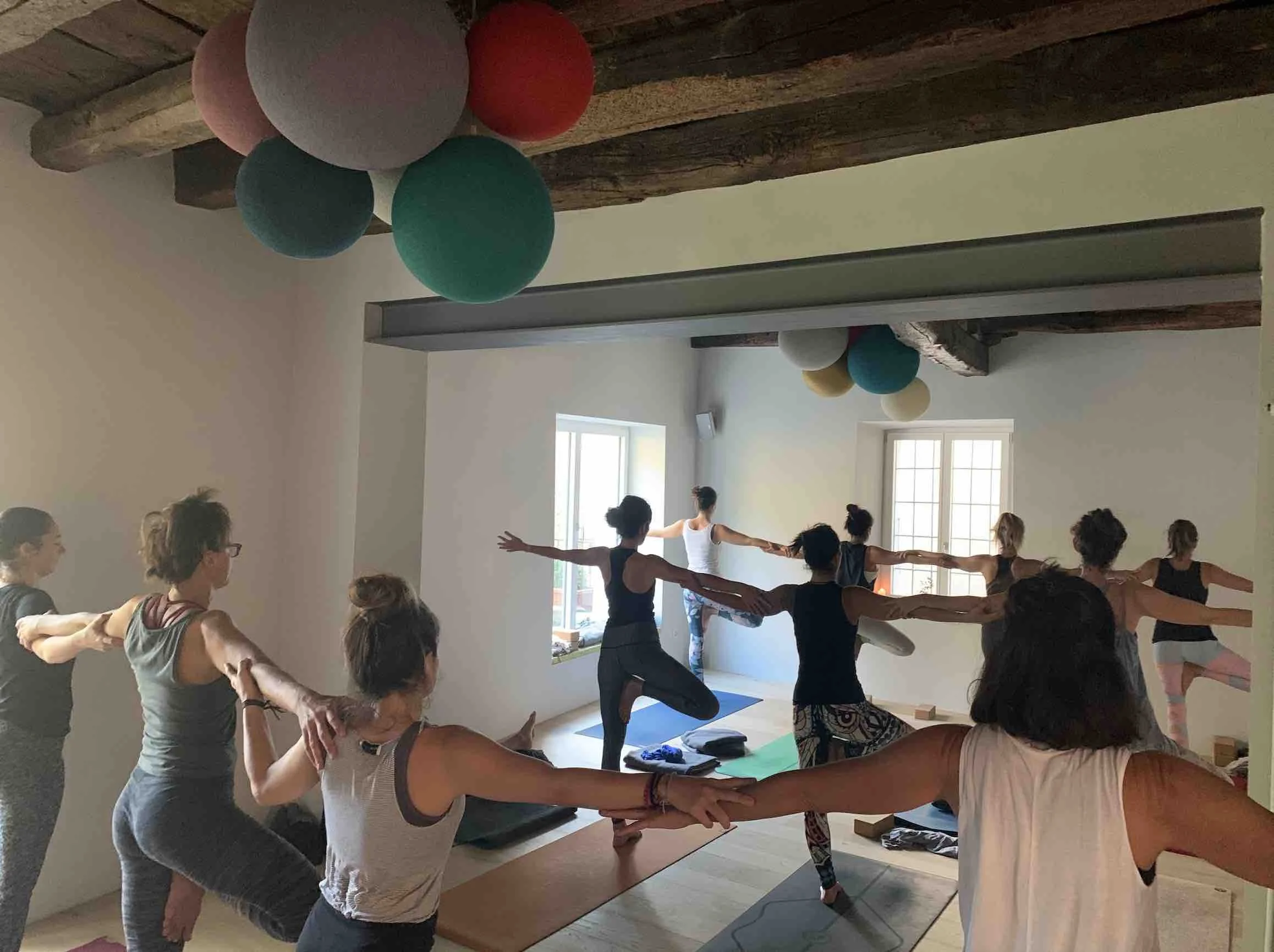 Gente che pratica yoga in una stanza luminosa con pareti bianche, illuminata da luce naturale, decorata con palloncini colorati
