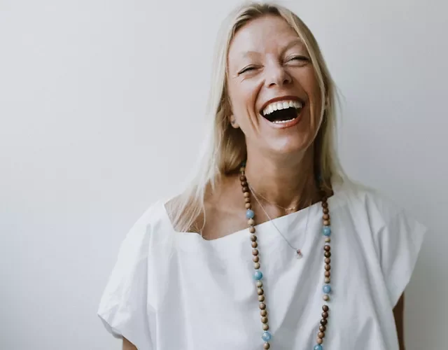 Donna sorridente con abito bianco e collana di perline, sfondo bianco.