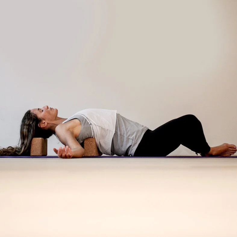 Donna che fa yoga su un tappetino, appoggiata sui blocchi, in posizione di rilassamento.