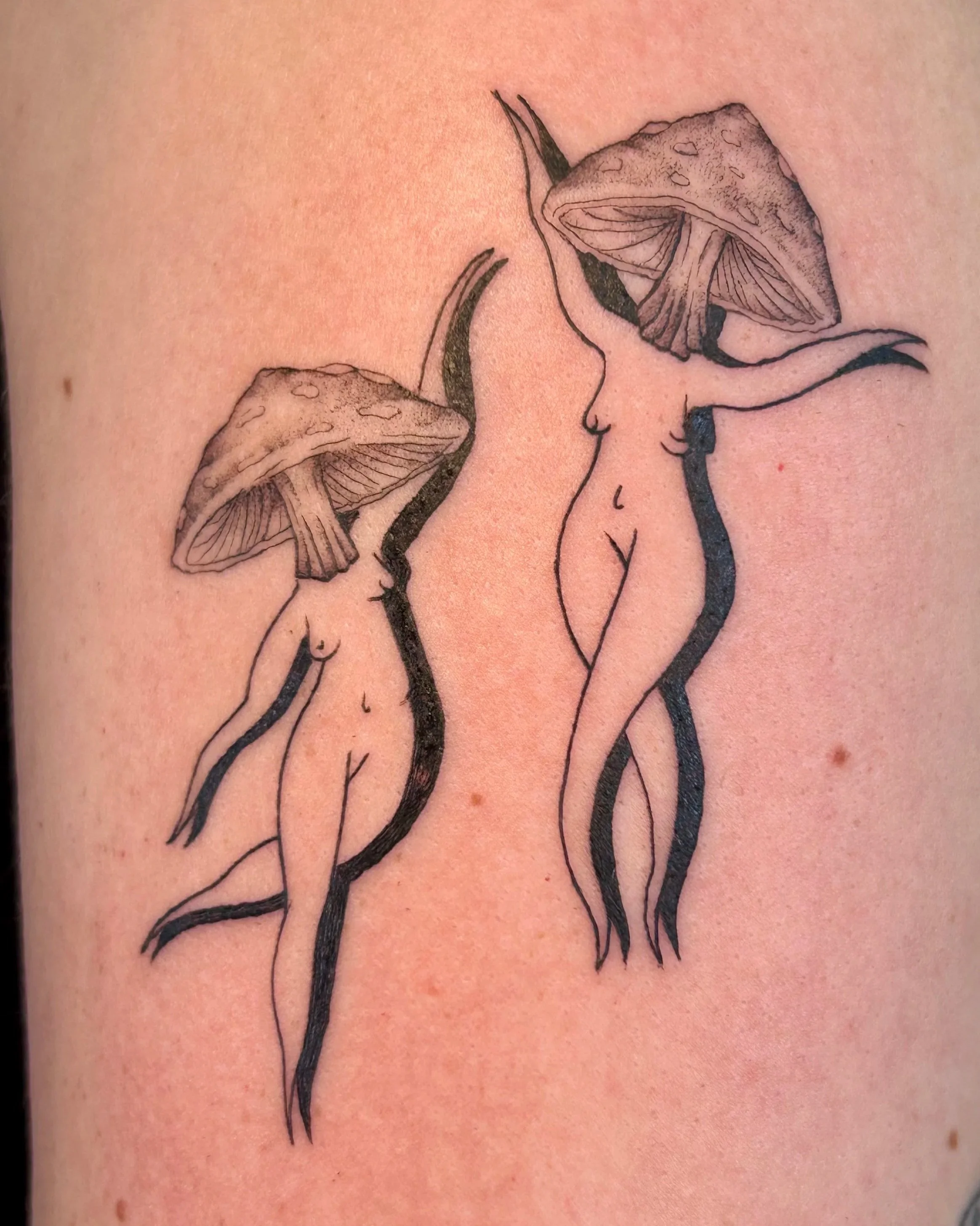 Verspieltes Fineline Tattoo mit zwei tanzenden Pilzfrauen als queer-fantastisches Motiv, gestochen im Tattoo Atelier in Konstanz am Bodensee
