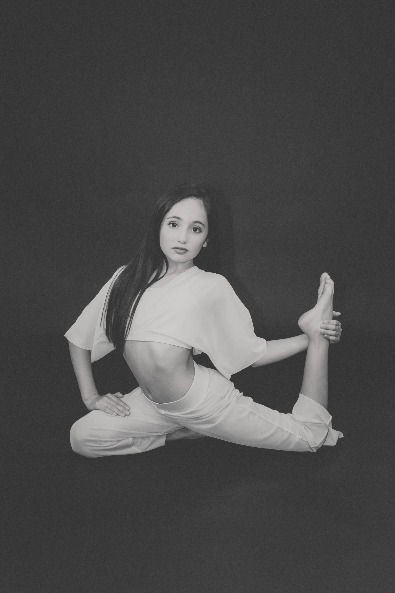 Young woman in white athletic clothing performing yoga pose against a dark background.