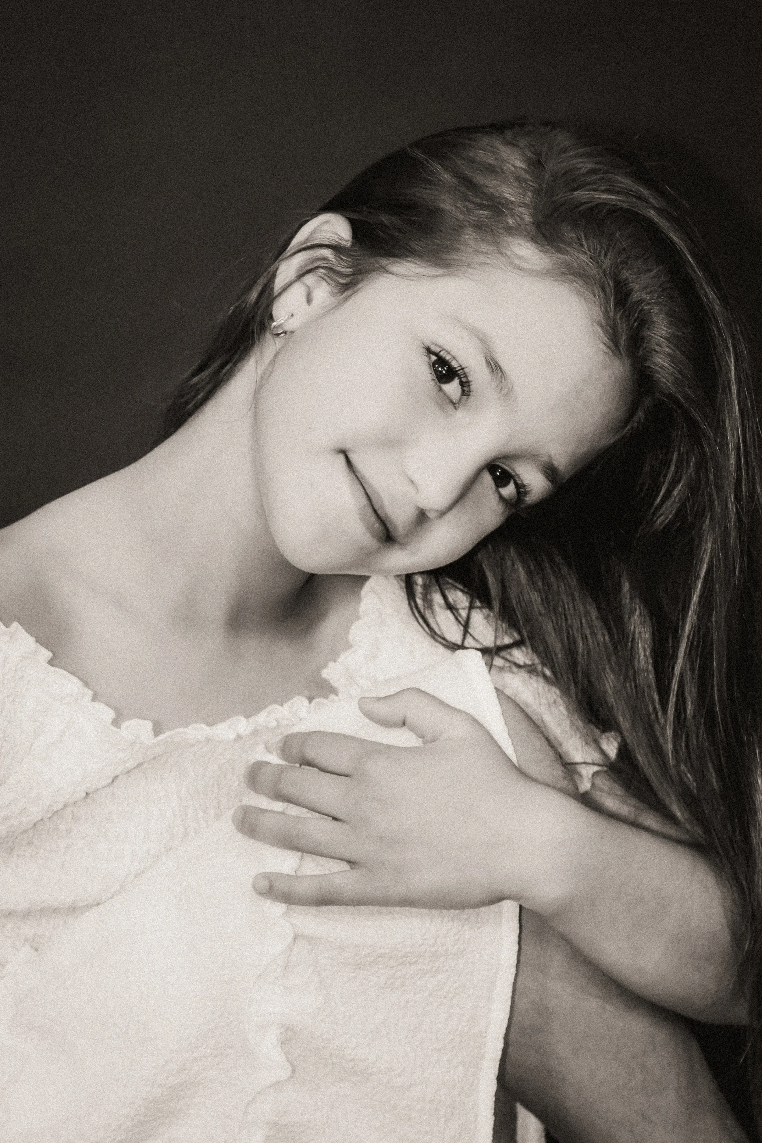 Black and white close-up photograph of a woman with long hair, smiling gently, wearing small earrings, wrapped in a soft, textured fabric.