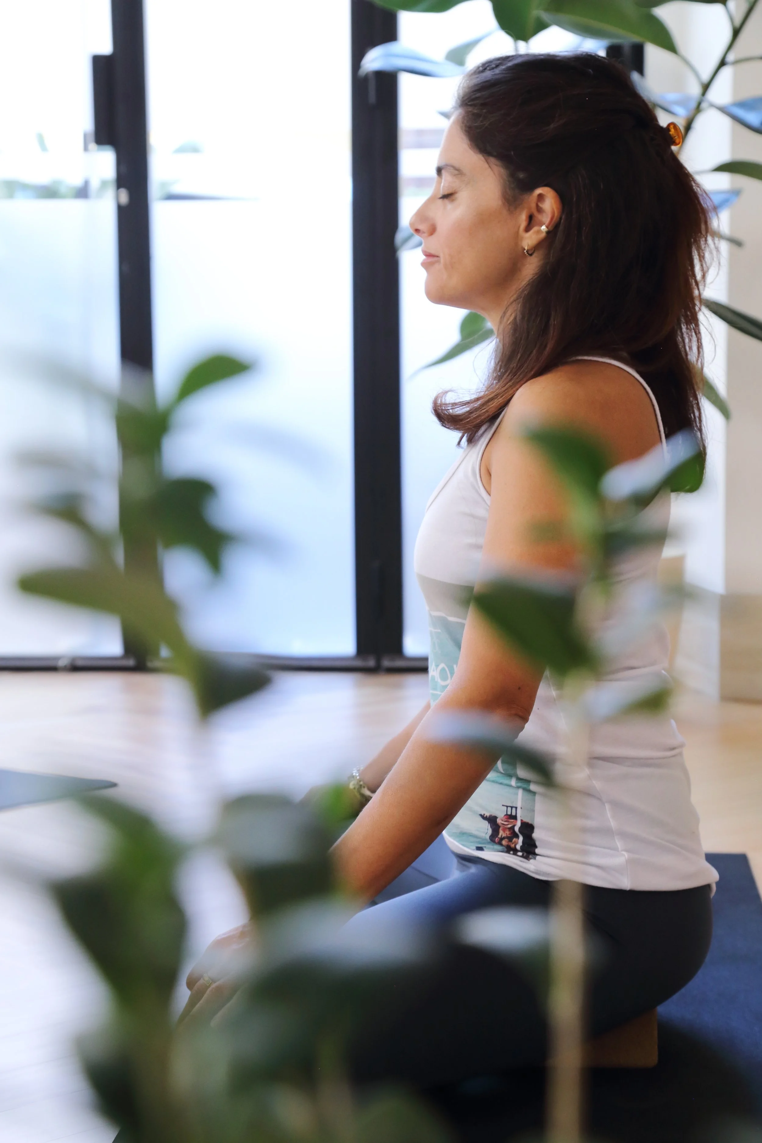 Una donna seduta in posizione di meditazione in un ambiente interno, circondata da piante verdi