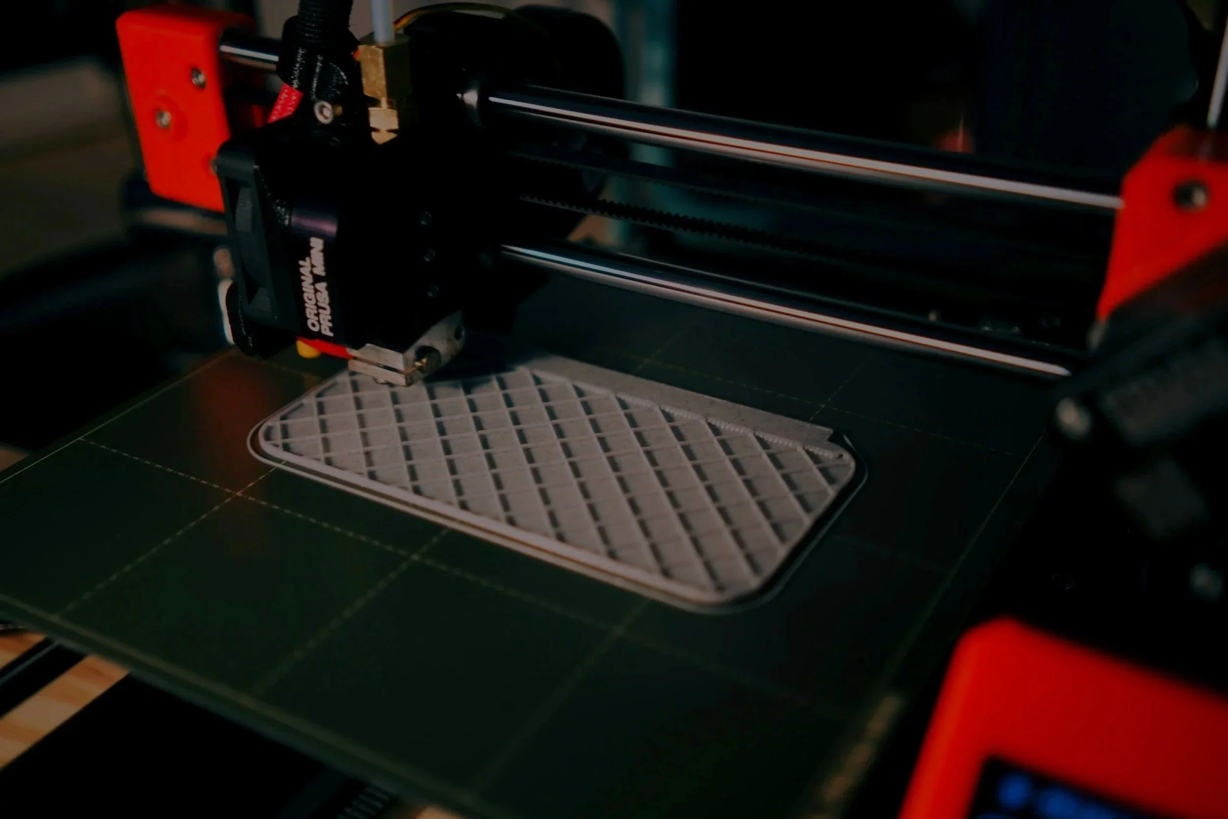 A 3D printer printing a gray, lattice-patterned object on a green printing bed.