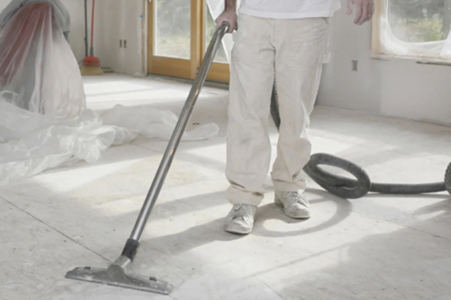 Persona che utilizza un aspirapolvere industriale per la pulizia di un pavimento durante i lavori di ristrutturazione di una casa.