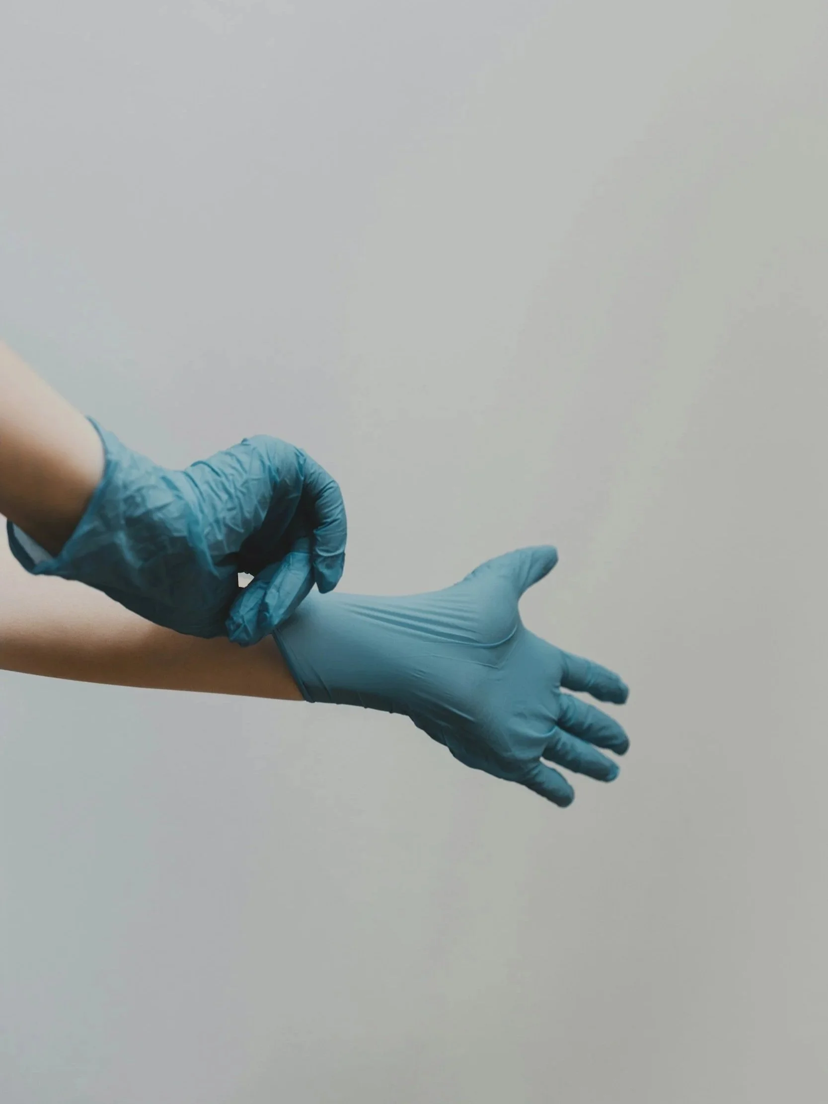 Una mano con un guanto blu si sta mettendo o togliendo da un altro braccio con un guanto blu, contro uno sfondo bianco.