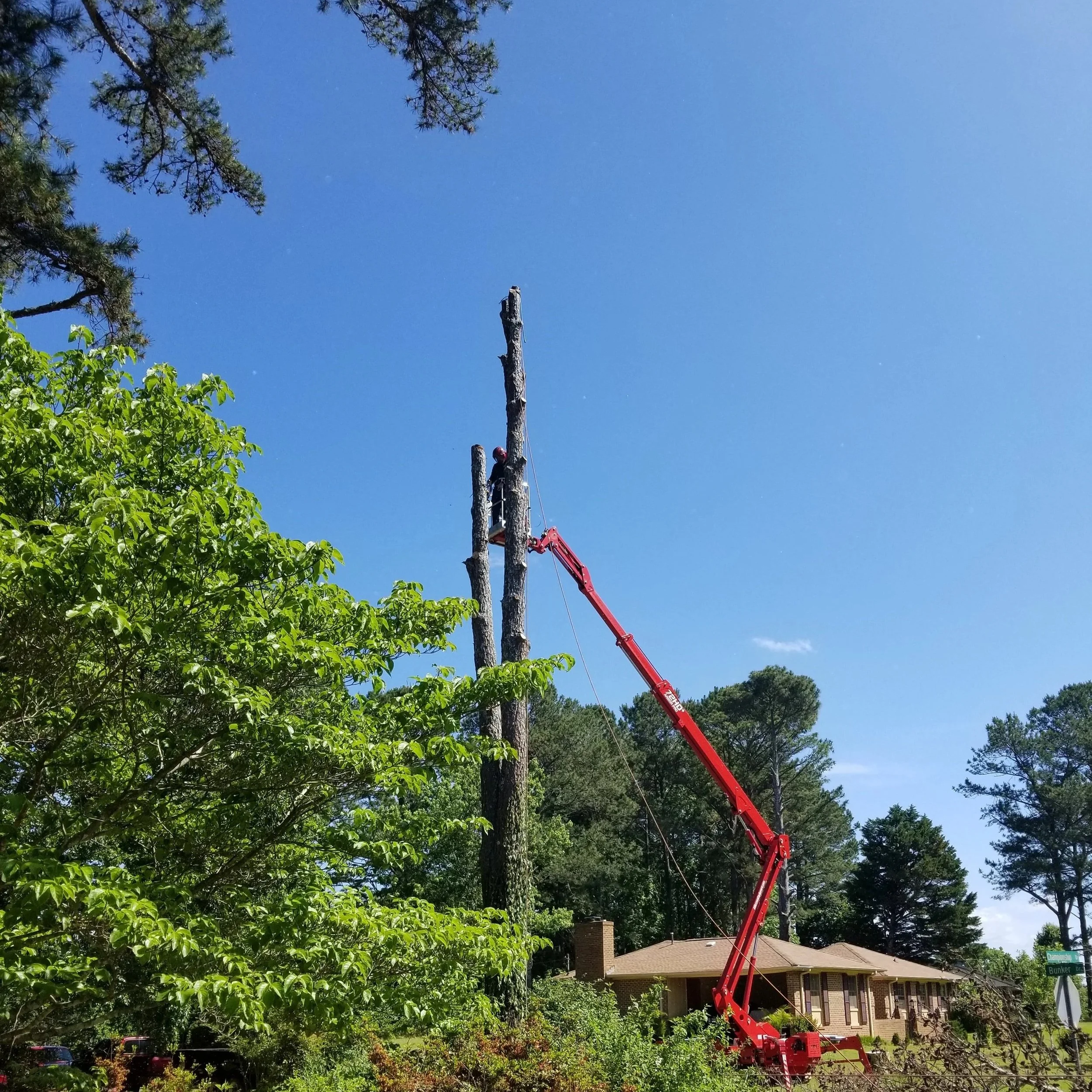 Worker in safety gear and helmet on a tall utility pole, using a cherry picker lift to perform maintenance or repairs.