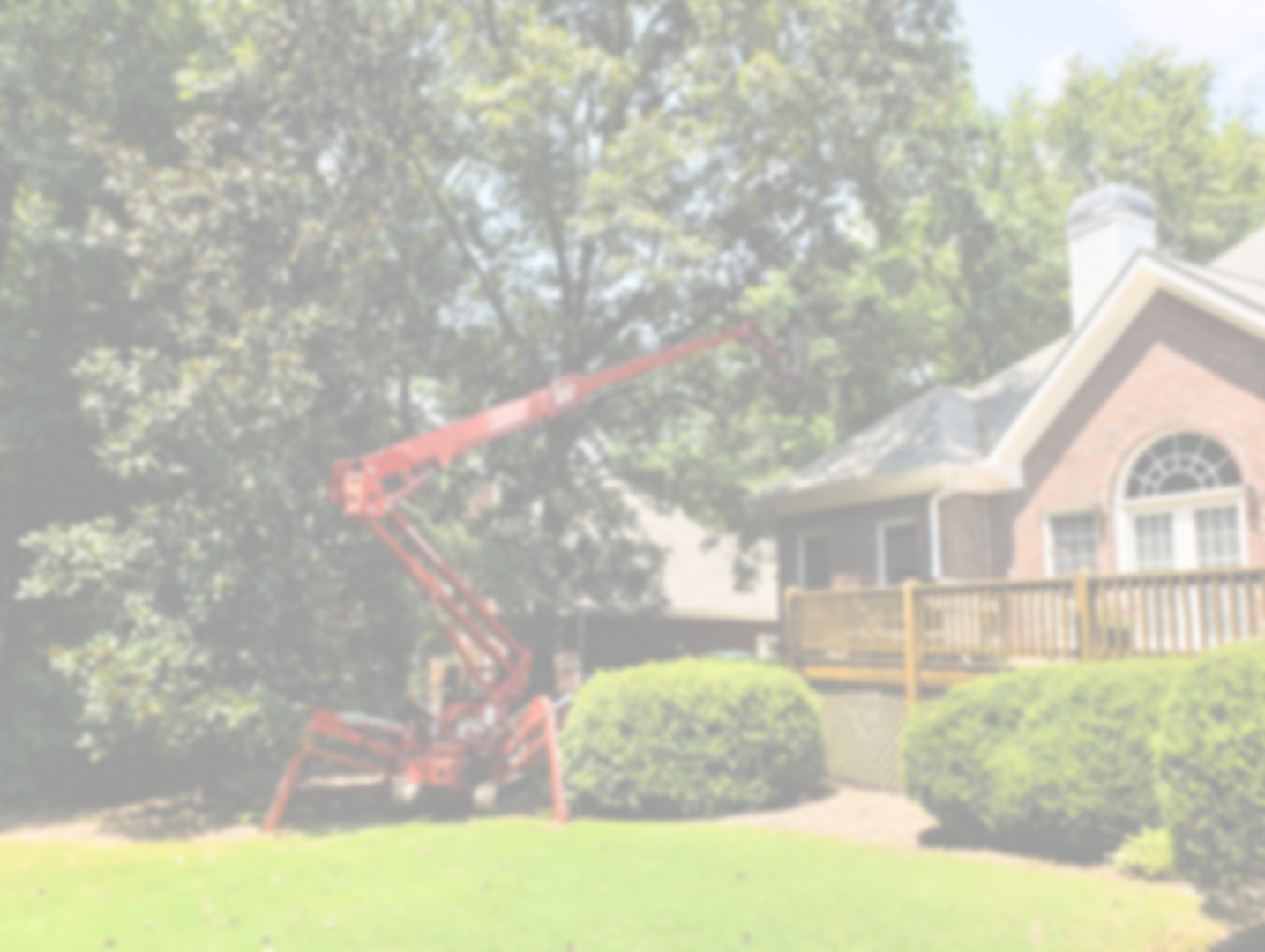A red lift pole extending from a bucket truck trimming a large tree in a residential yard, with a brick house, a wooden deck, and green bushes in the background.
