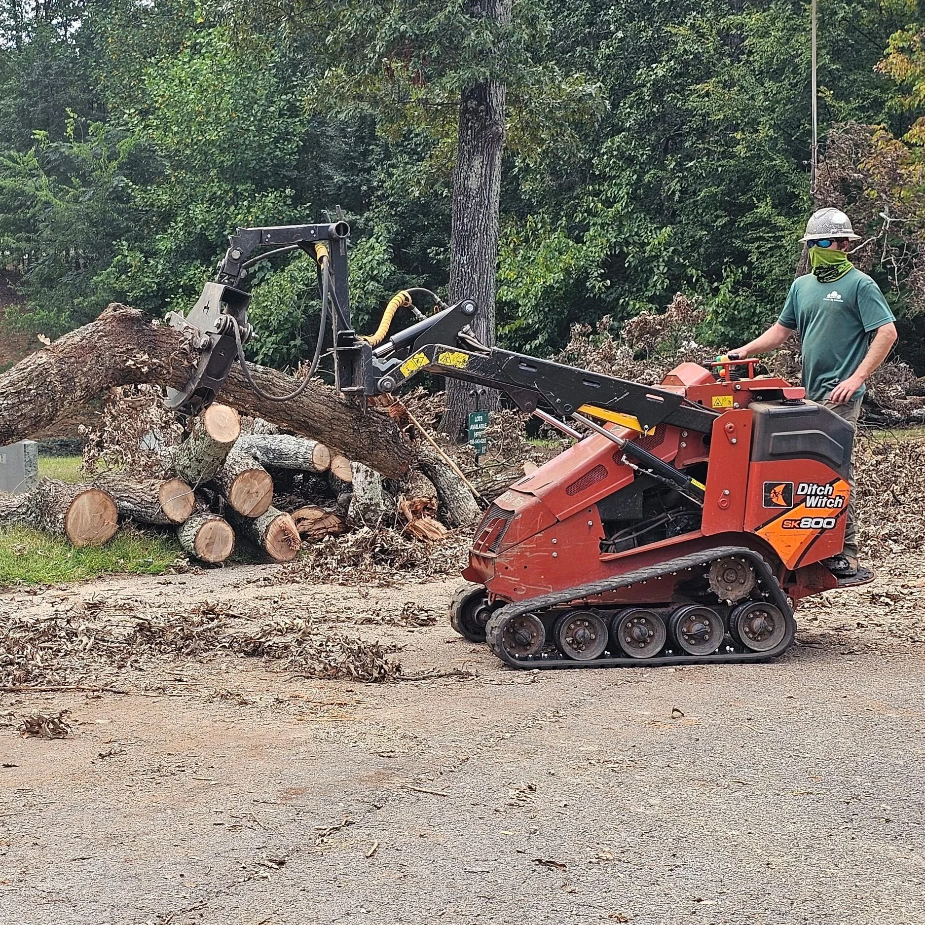 A person operating a tracked wood chipping machine to process a fallen tree in a wooded area.