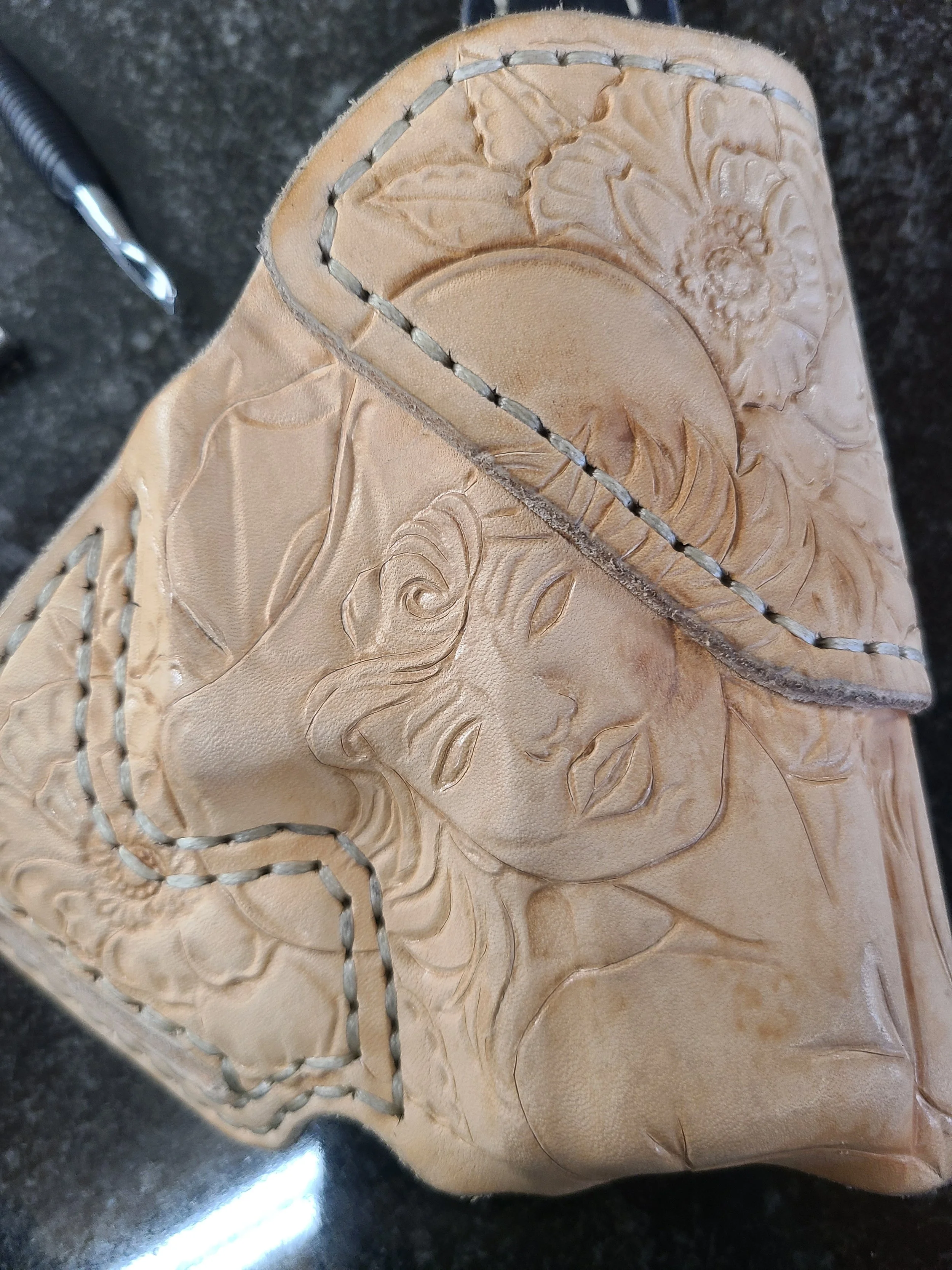 Leather wallet with embossed floral and female face design, stitched edges, lying on a dark surface.