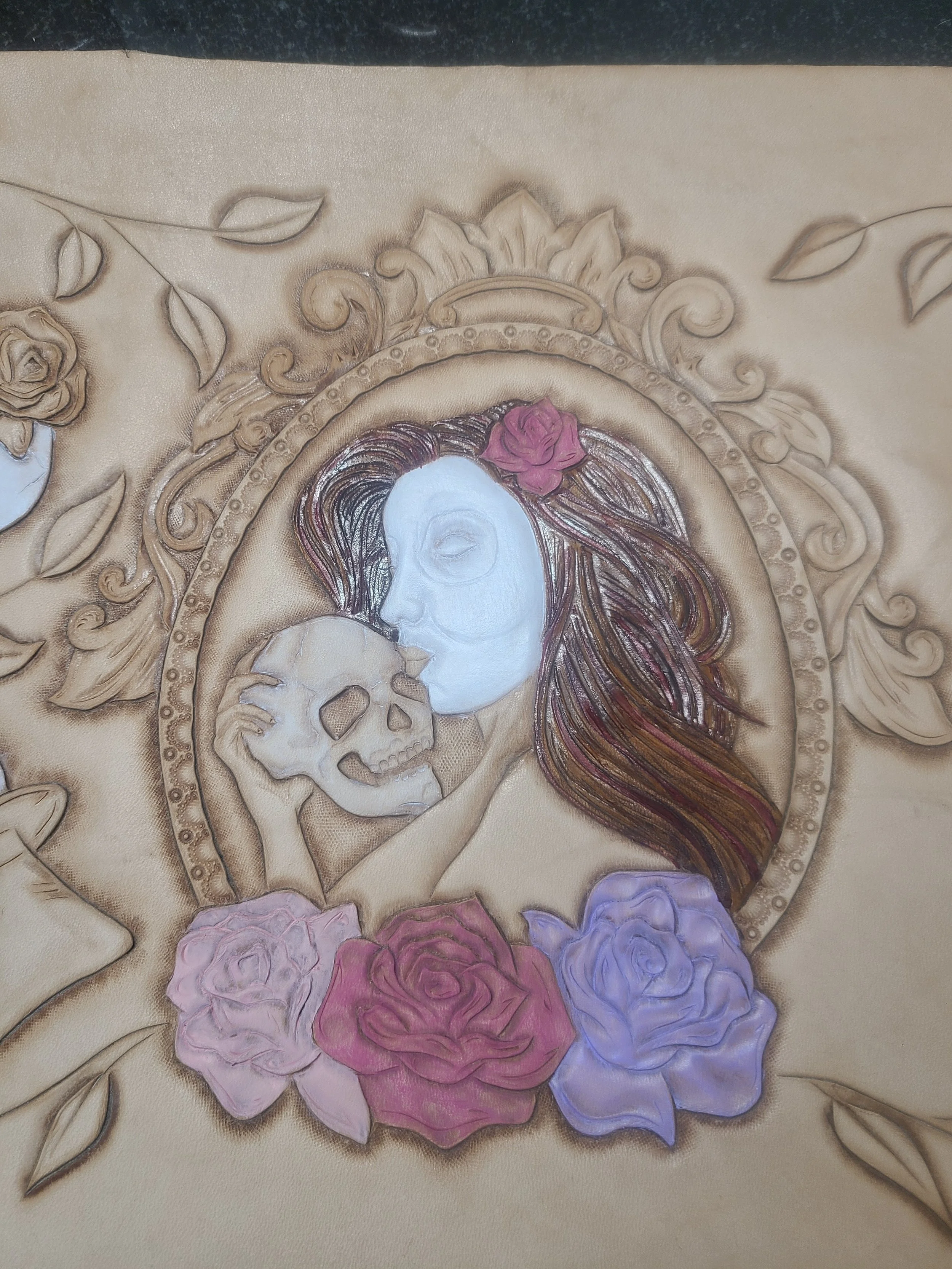 An artistic portrait of a woman with long, flowing hair adorned with a pink rose, holding a skull close to her face. The background features ornate gold and floral embellishments.