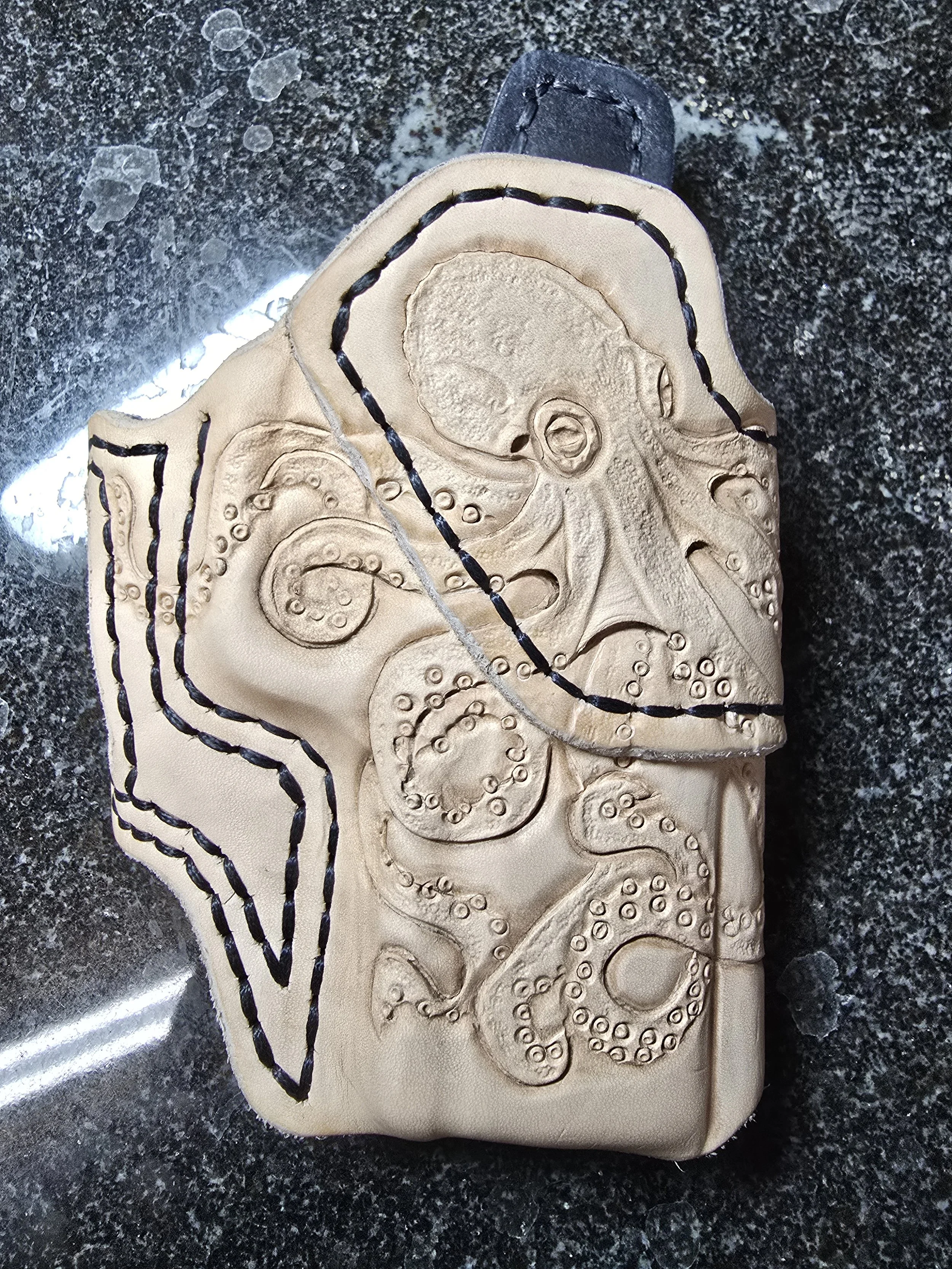 Leather phone case with embossed octopus design and black stitching on a dark granite surface.