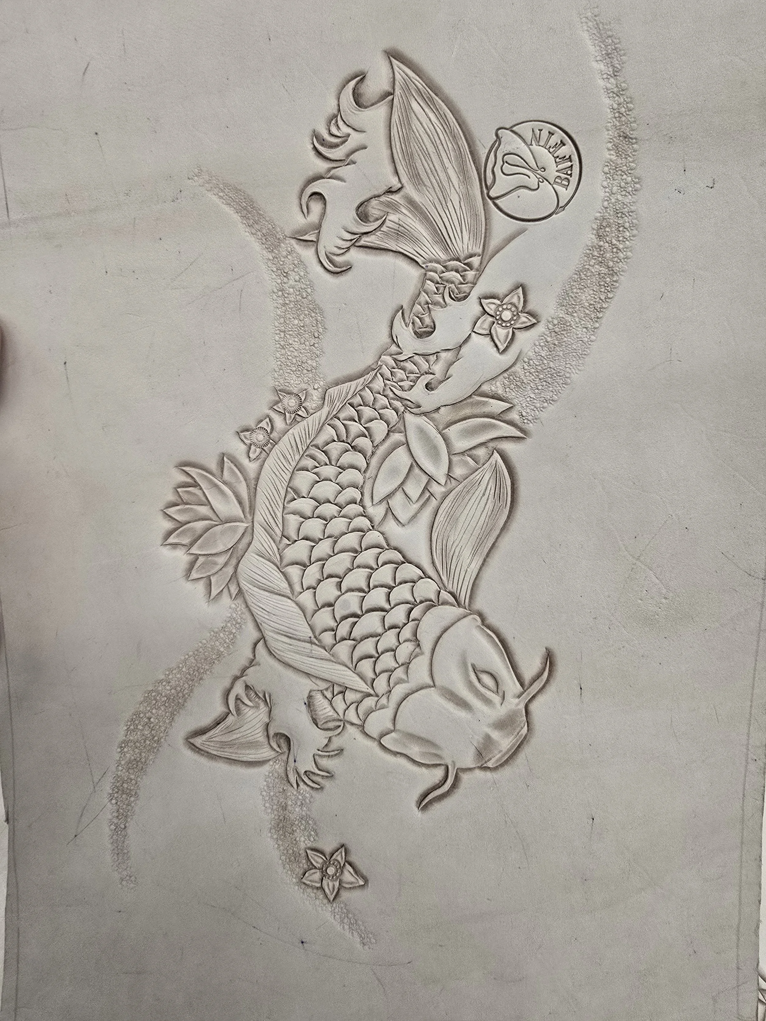 A detailed pencil drawing of a koi fish with flowers, leaves, and a circular emblem that says 'NILKAI' and 'BASK'.