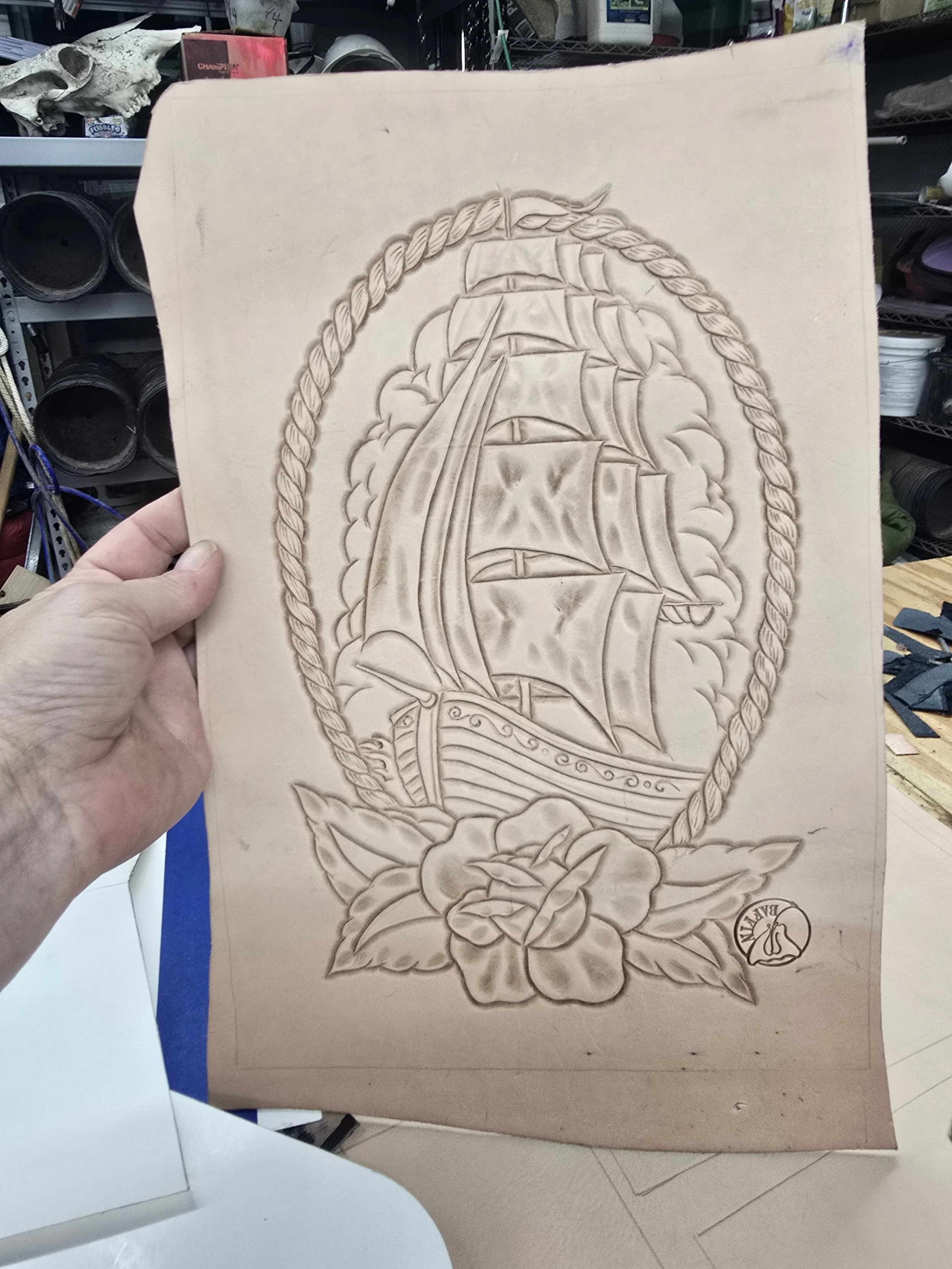 Wooden carving of a ship with sails, surrounded by a rope border and a flower at the bottom right corner with the word "BAYON".