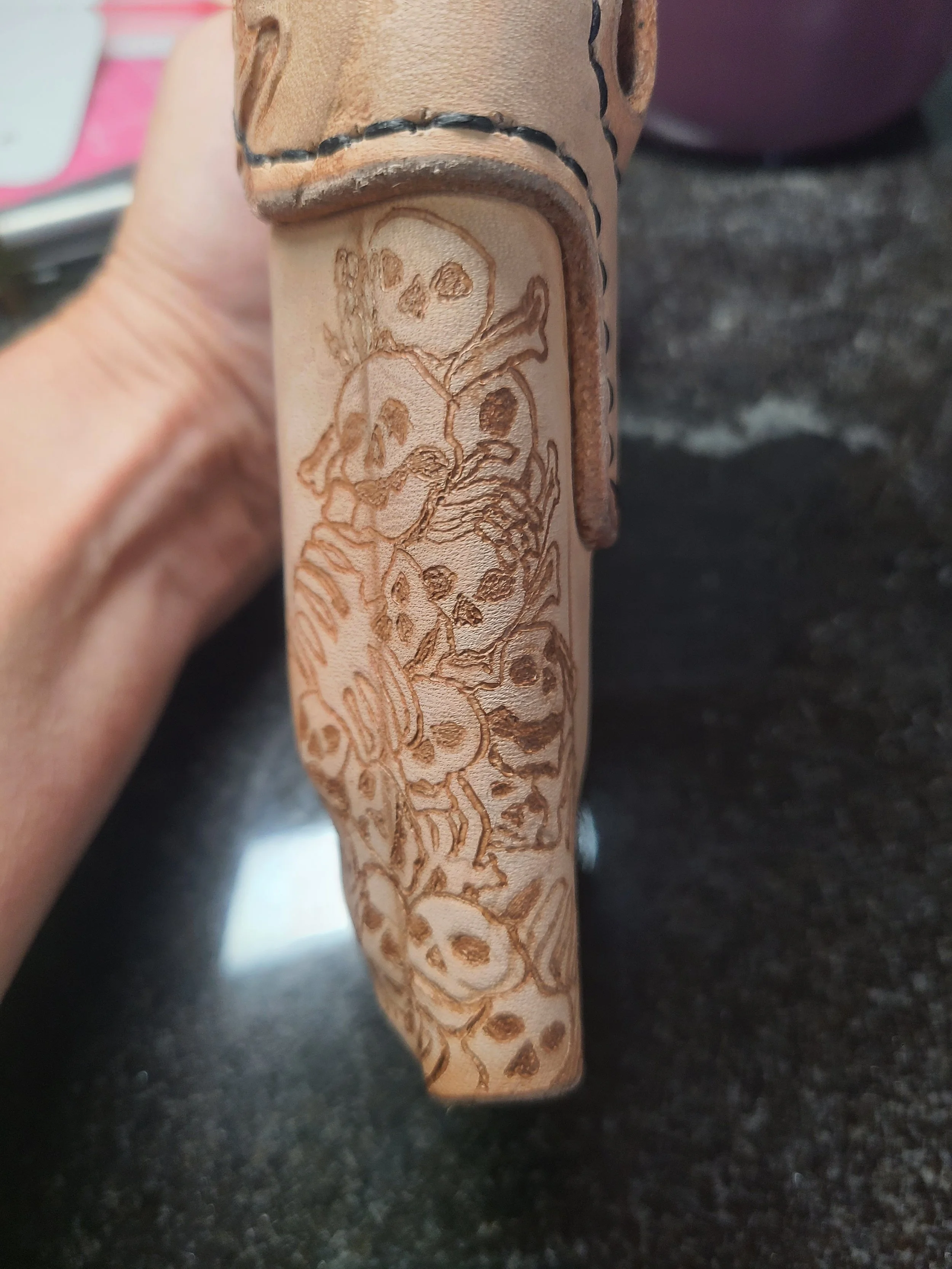 Close-up of a leather item with a floral skull design engraved on it.