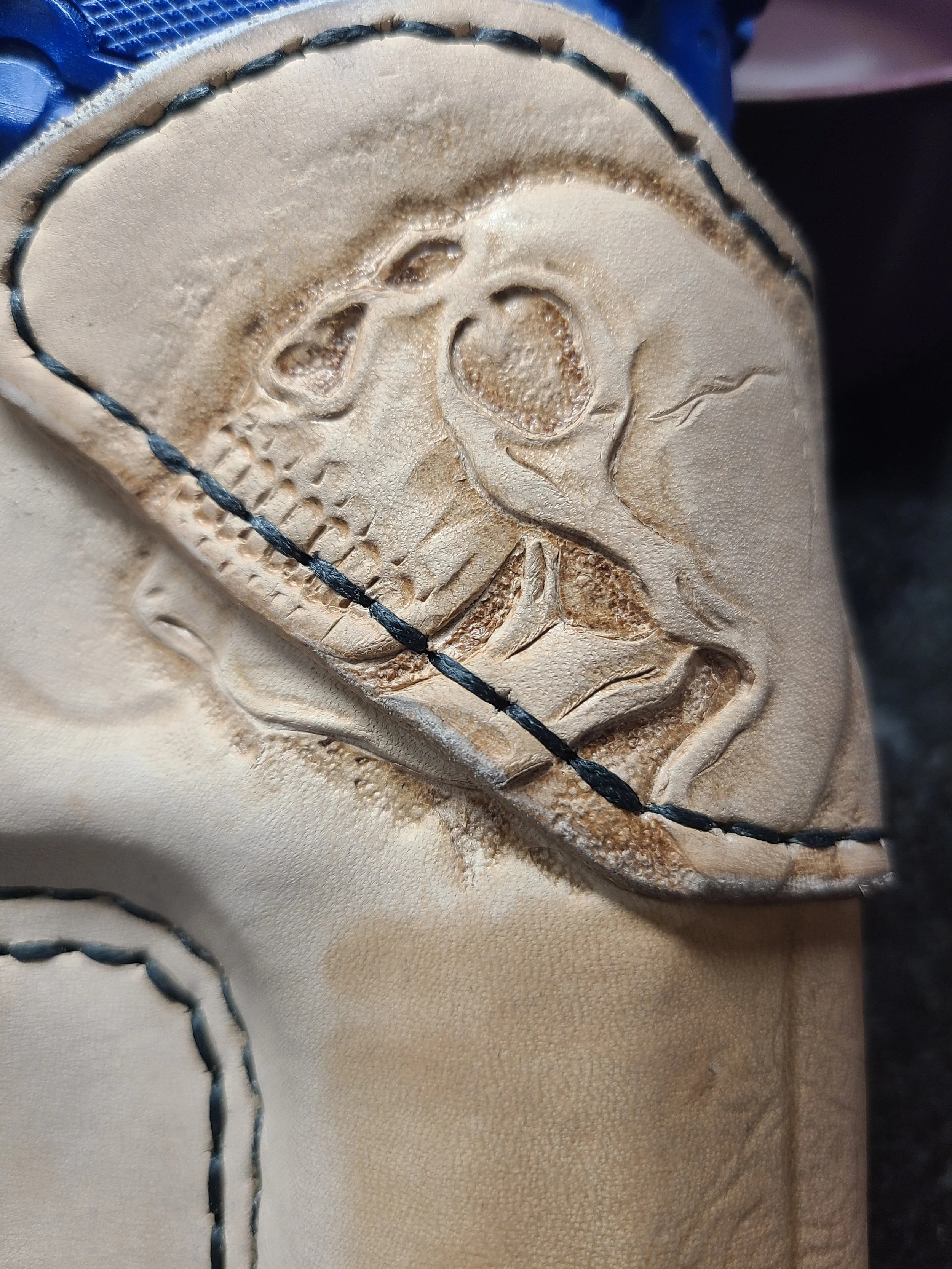 Close-up of a beige baseball glove with a skull and rose design embossed on the leather, stitched with black thread.