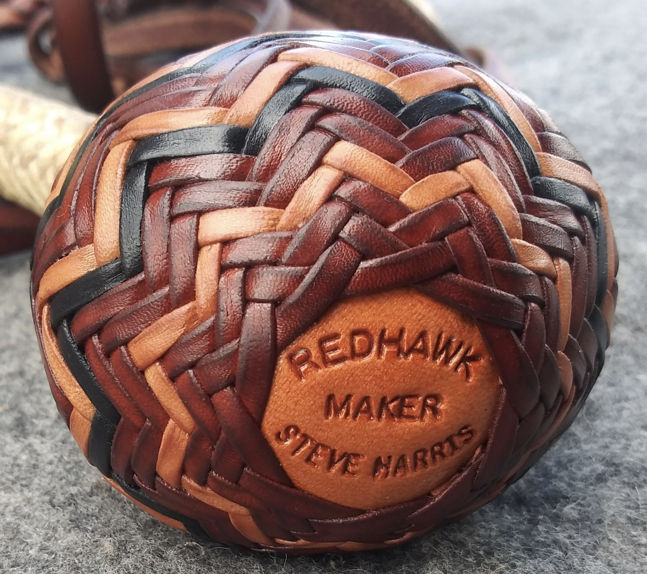 Close-up of a woven leather ball with a leather patch engraved with 'REDHAWK MAKER STEVE HARRIS'.