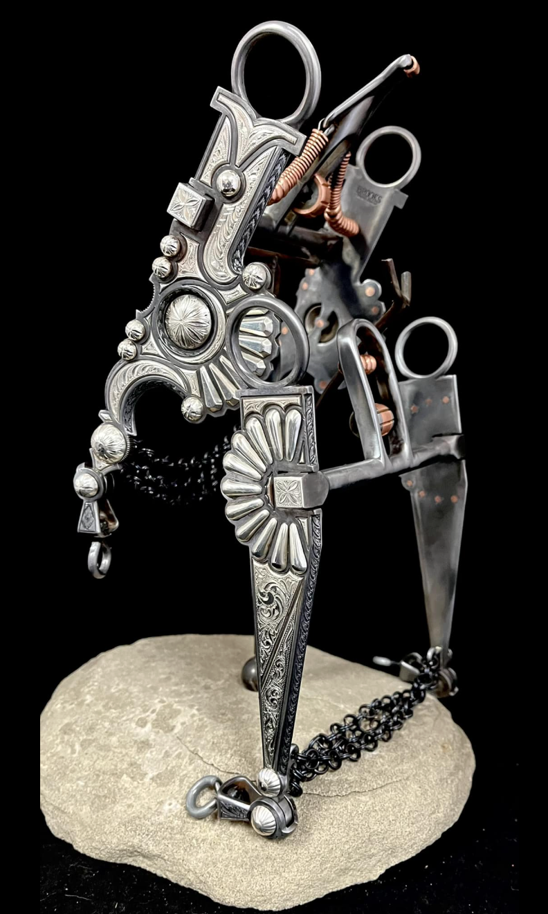 A sculpture resembling a gun, made from metal parts with ornate engravings, set on a rock with a black background.