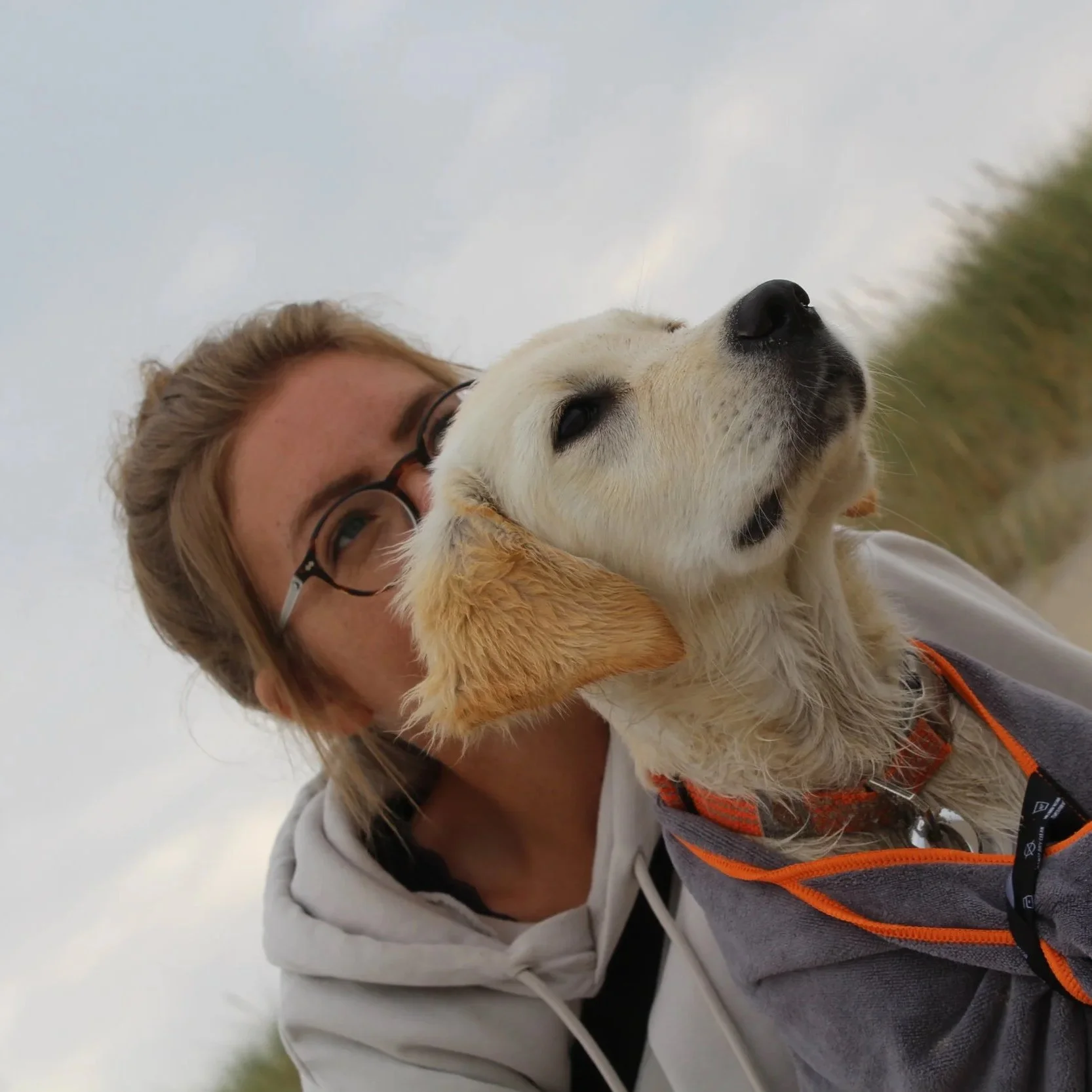 Eine Frau mit Brille hält ein süßes Golden Retriever Welpen im Arm, draußen bei bewölktem Himmel.