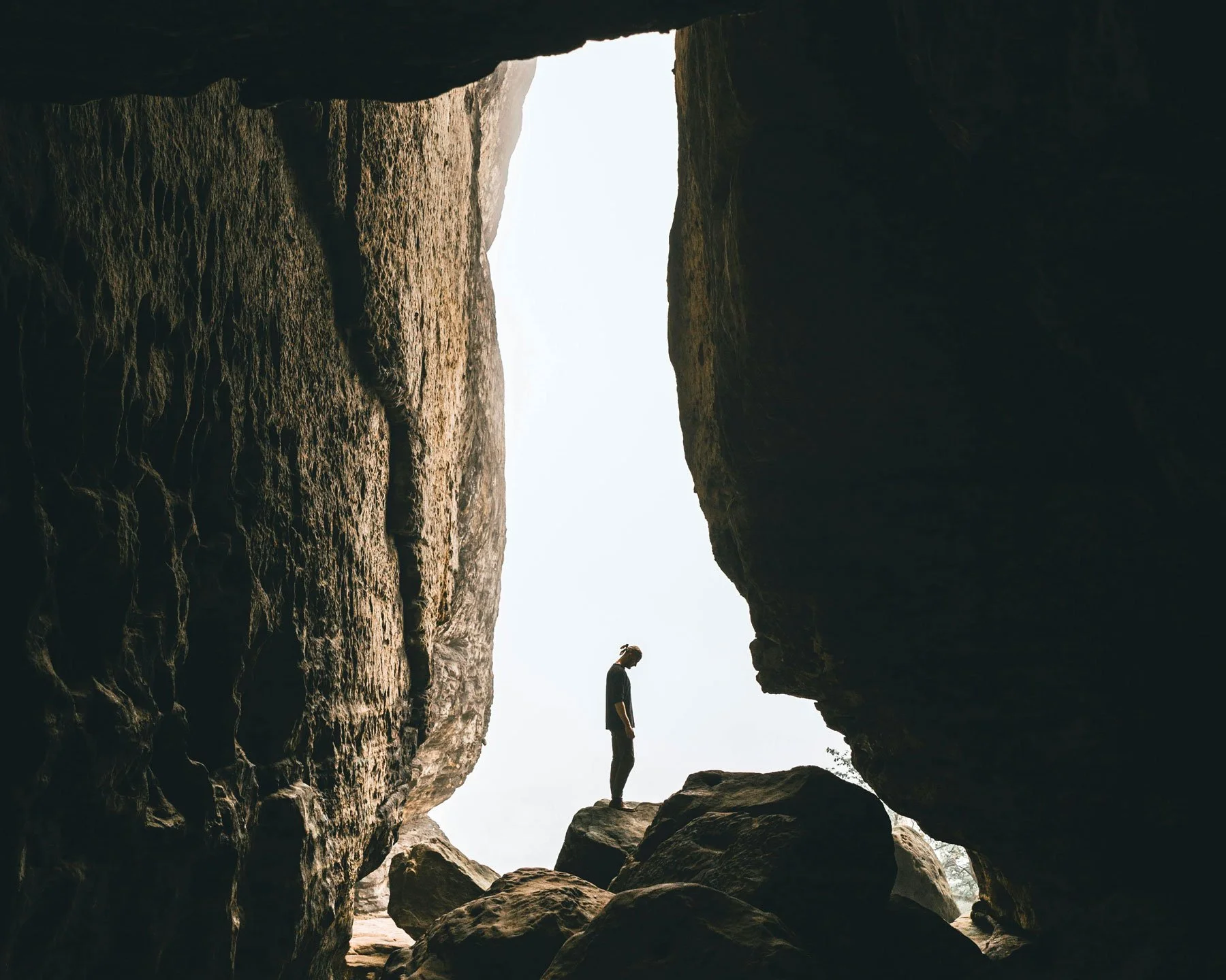 Person standing silhouetted in the opening of a dark cave looking out toward light, representing the limits of analytical thinking and the moment a leader recognises they cannot see past their own patterns