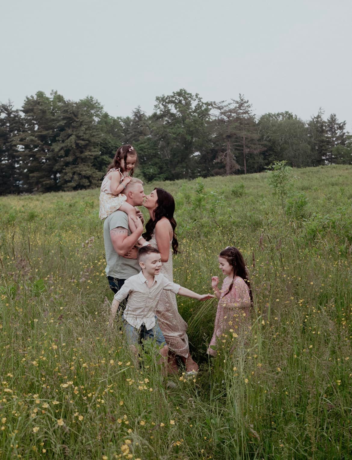 Family of six enjoying a playful moment in a grassy field during daytime, with trees in the background.