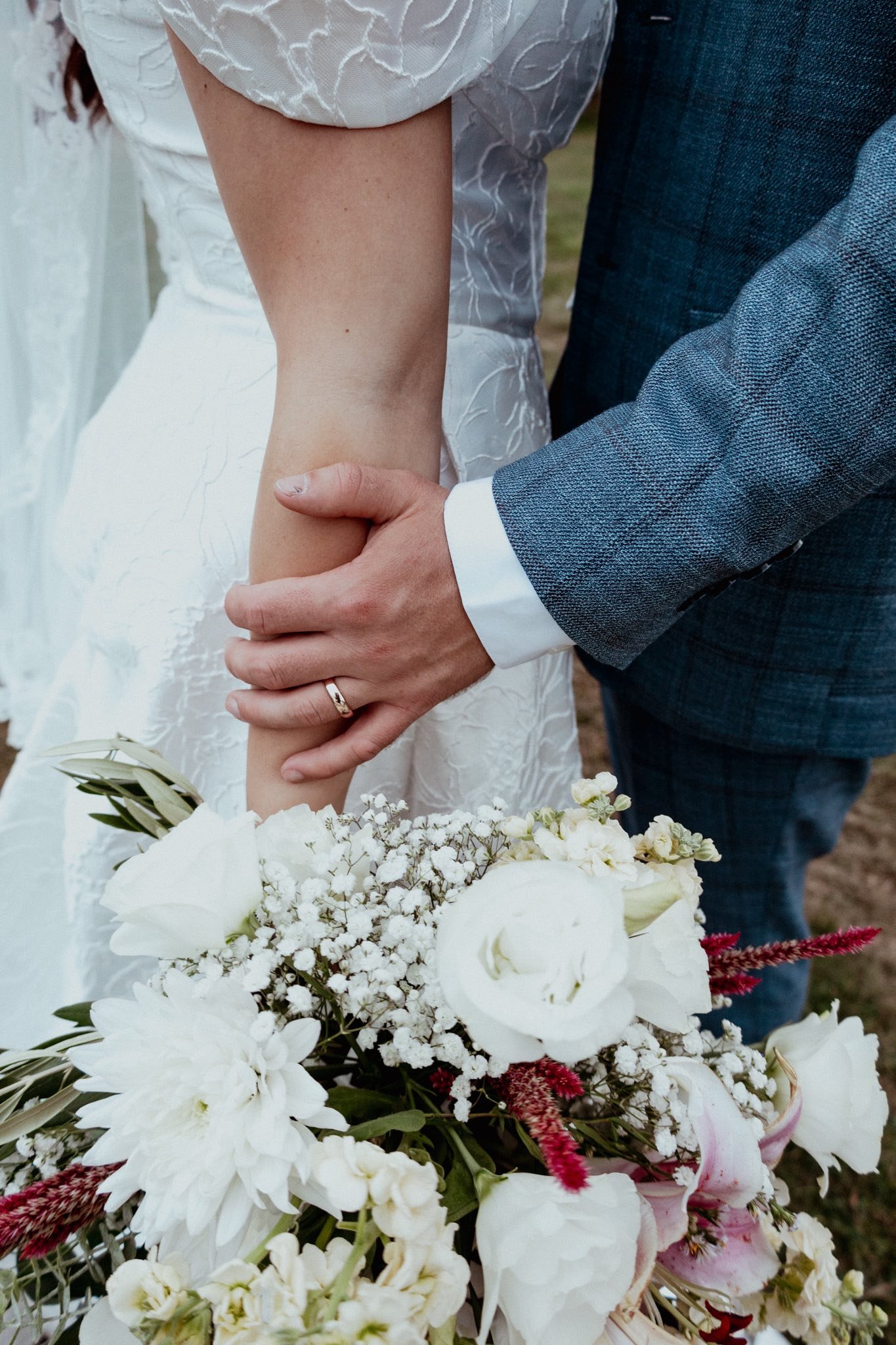 A couple dressed in wedding attire holding hands with a bouquet of white flowers.