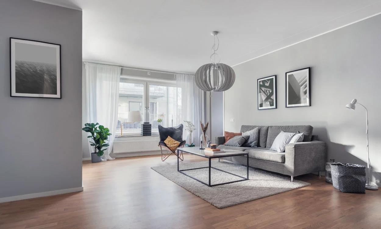 Modern living room with a gray sofa, black armchair, coffee table, framed black and white art, potted plant, and natural light from large windows.