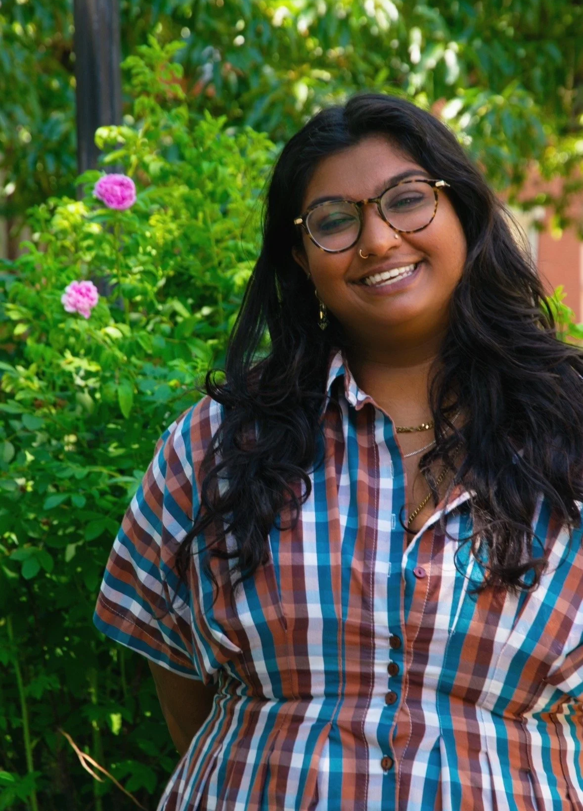 Warm and affirming Indian therapist smiling in front of flowers.