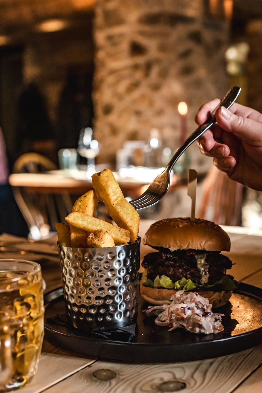 A burger with fries and coleslaw on a black tray at a restaurant