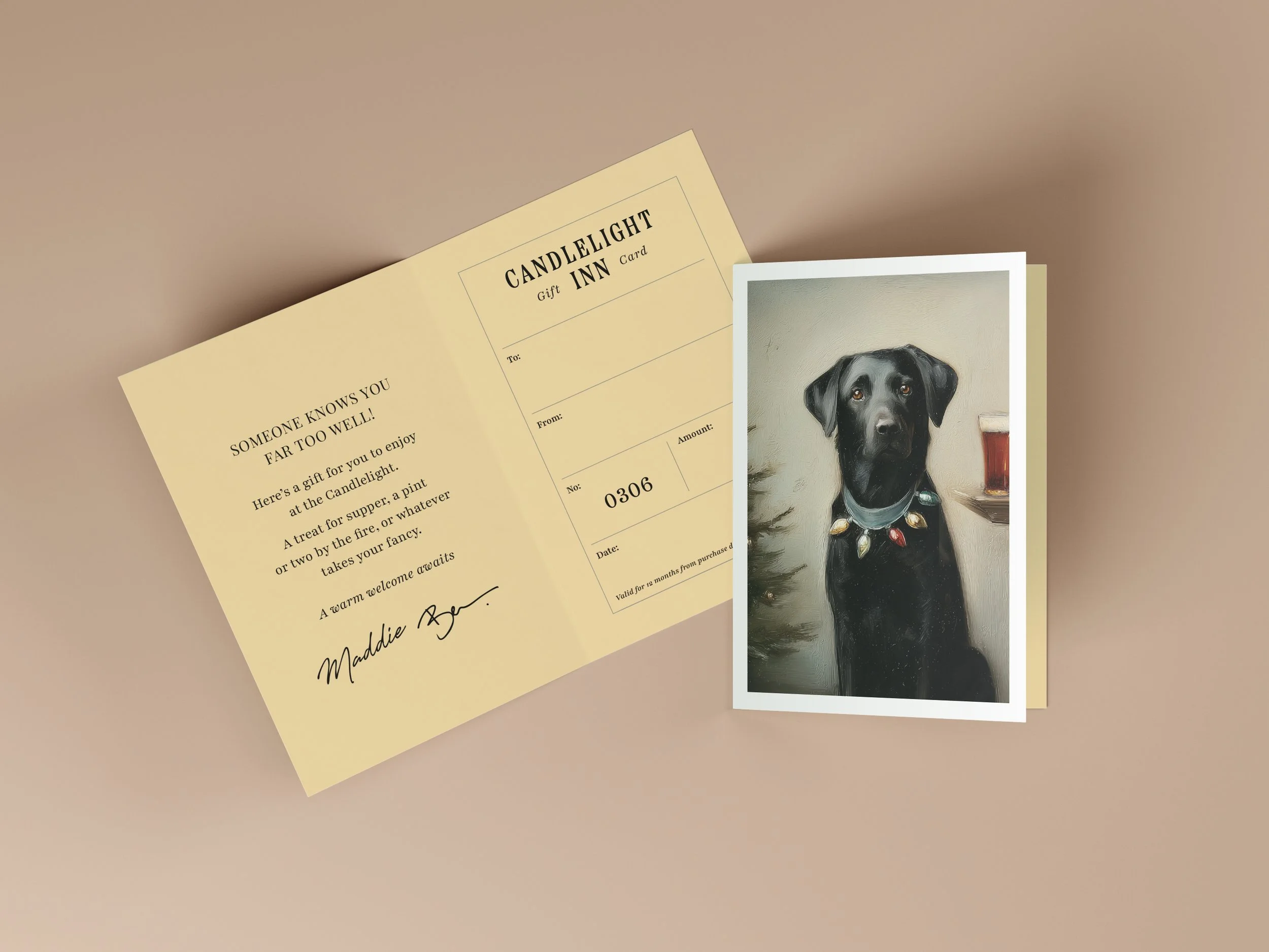 A greeting card and a photograph of a black dog wearing a collar with decorative charms, next to a glass of dark beverage, on a beige surface.
