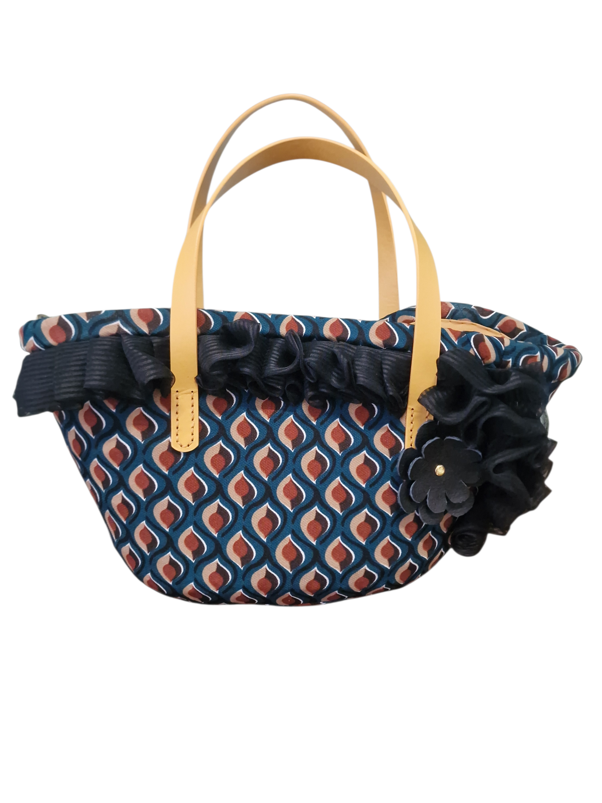 Vista frontale della coffa Vendicari: tessuto geometrico, manici in pelle color miele e Fiore Ammuri applicato a mano.