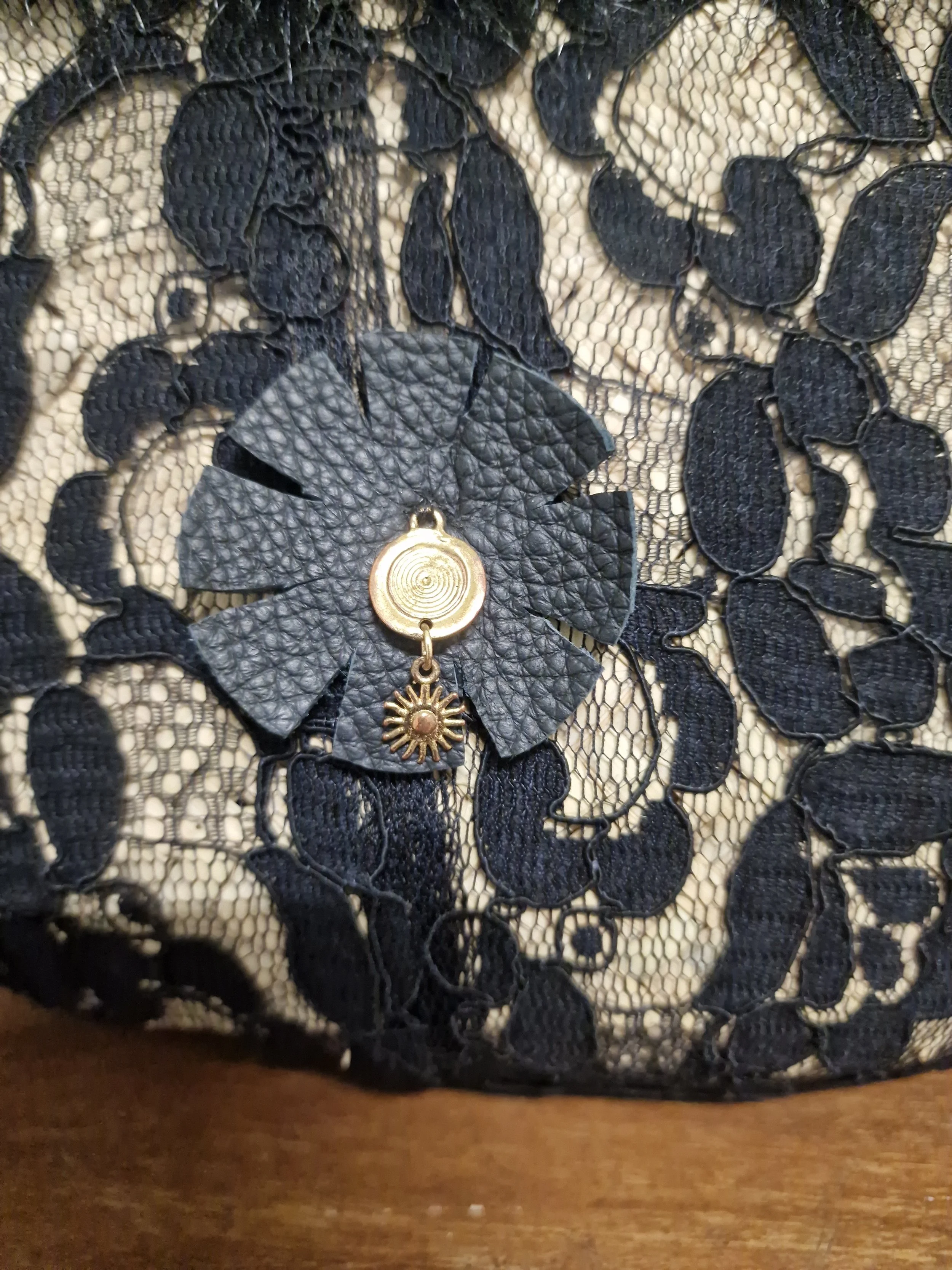 dettaglio del retro della borsa coffa che ha un fiore in pelle nera naturale con ciondolo in metralo dorato