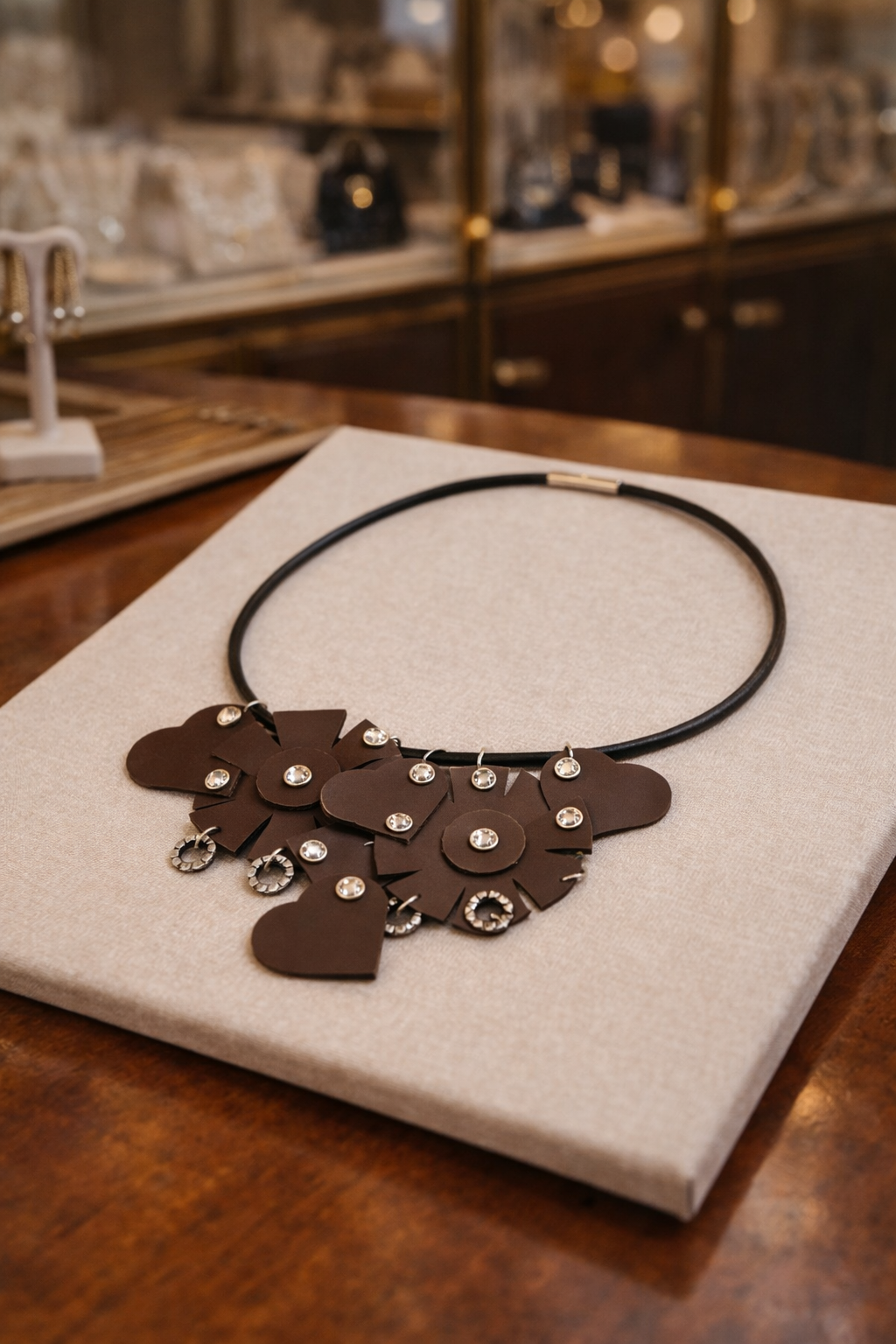 Collana Ammuri Noir appoggiata su base chiara su tavolo in legno con sfondo gioielleria sfocato.