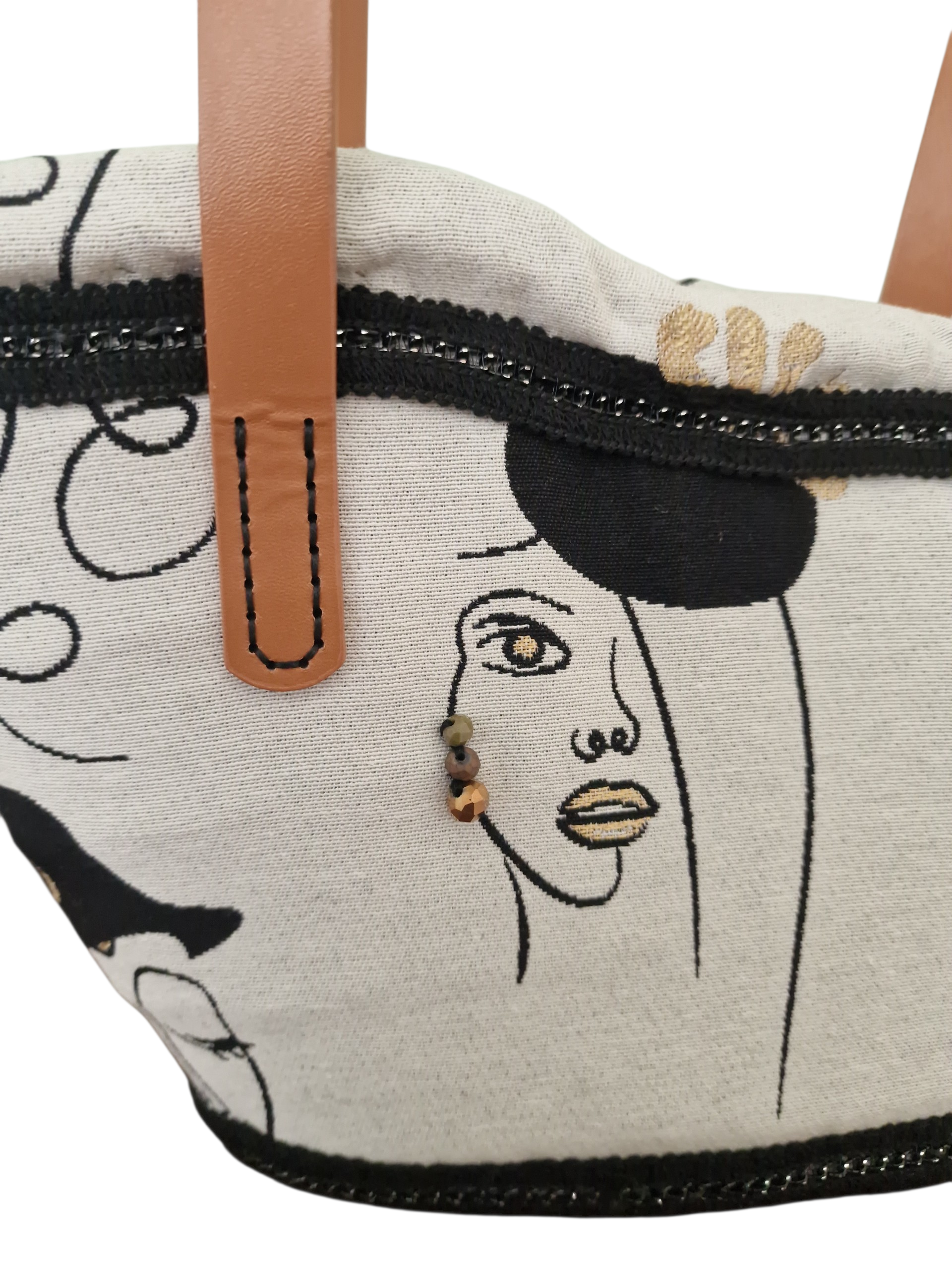 Dettaglio tessuto artistico con volti femminili e cristalli applicati come orecchini sulla coffa Ragusa