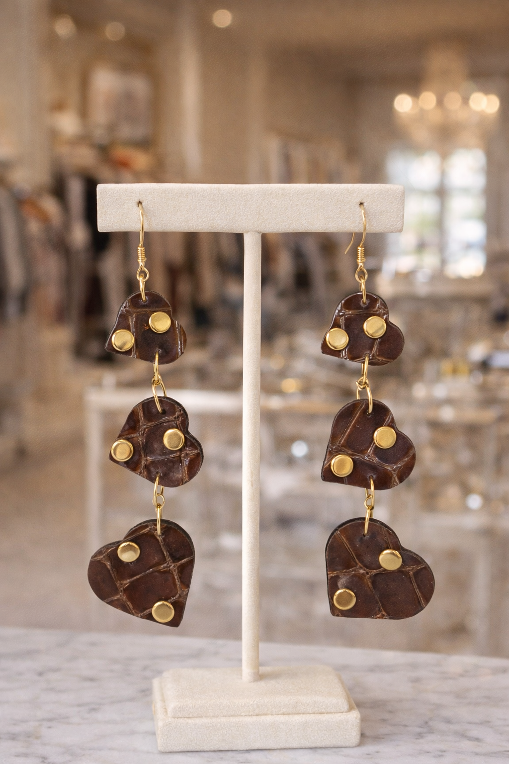 Orecchini pendenti con cuori in pelle effetto cocco marrone esposti su supporto elegante con dettagli dorati Ammuri Sicilia