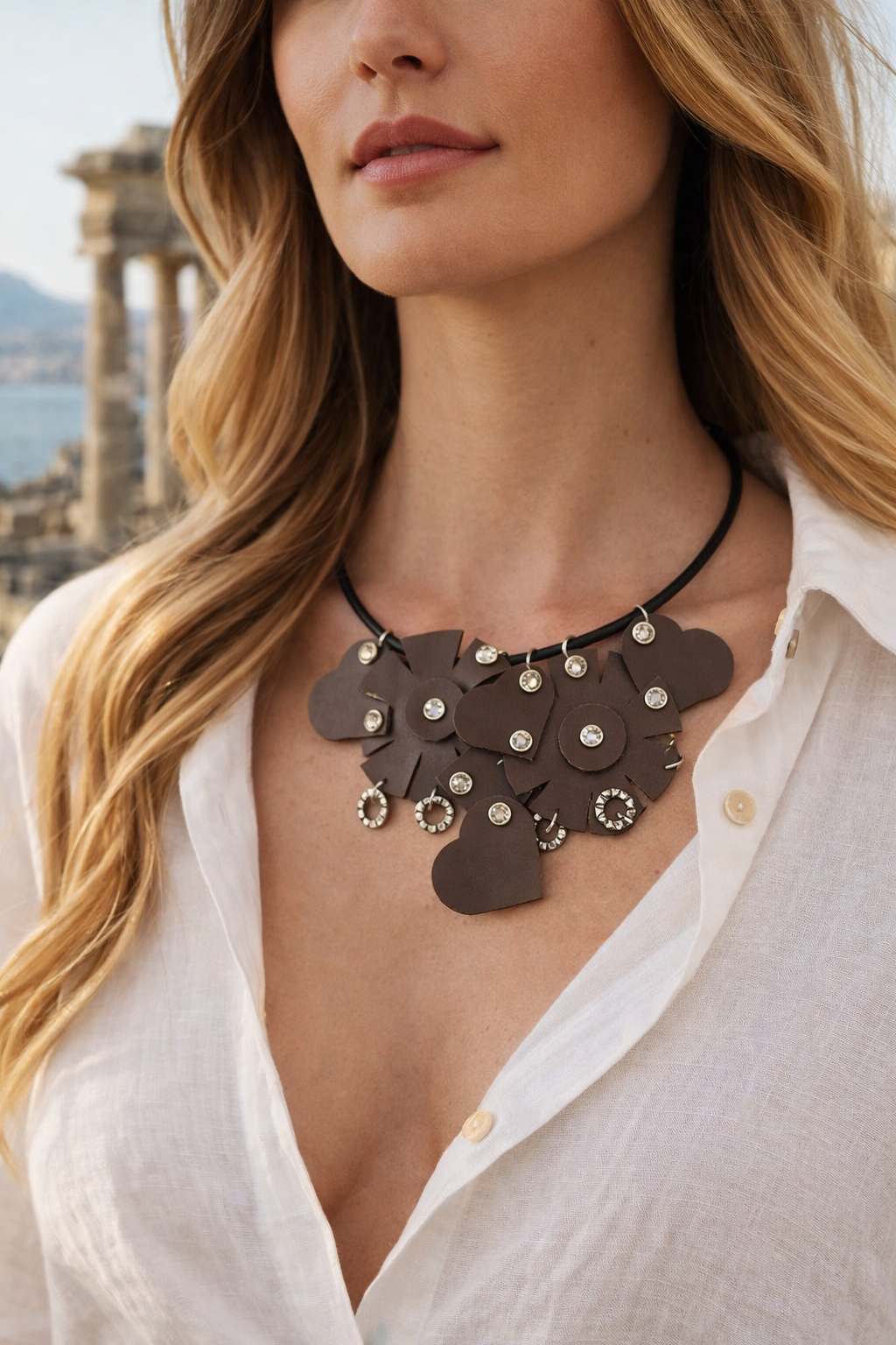 Collana Ammuri Noir indossata da modella con camicia bianca, ambientazione siciliana con mare e rovine sullo sfondo.