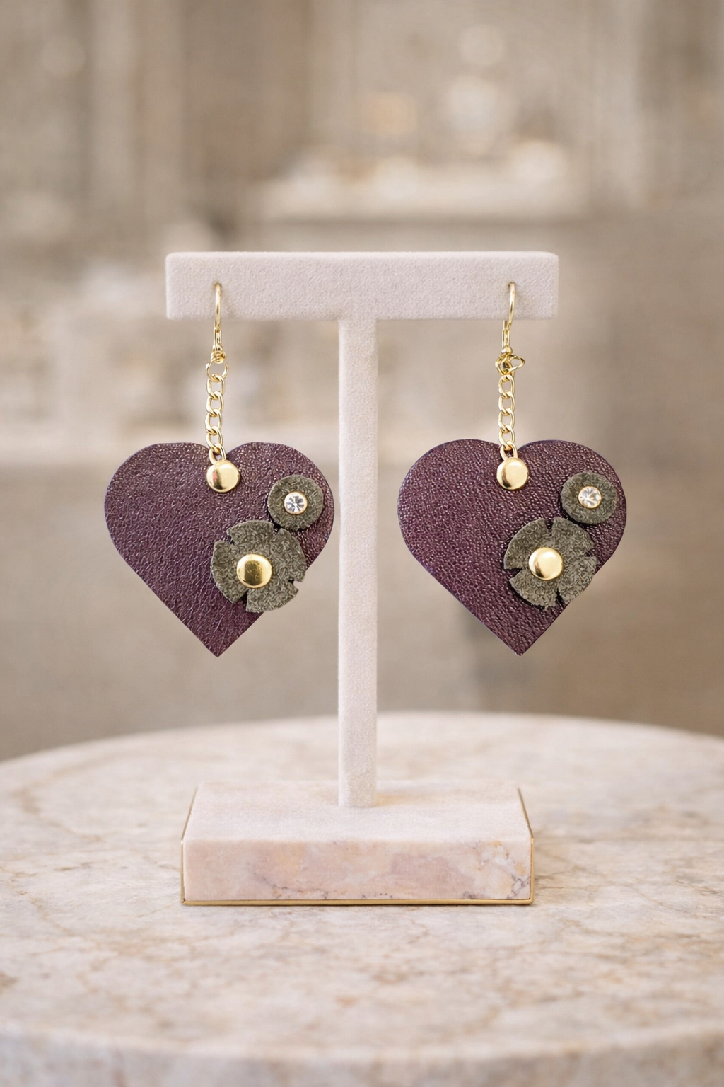 Orecchini artigianali a cuore in pelle bordeaux con fiore e dettagli oro su espositore elegante