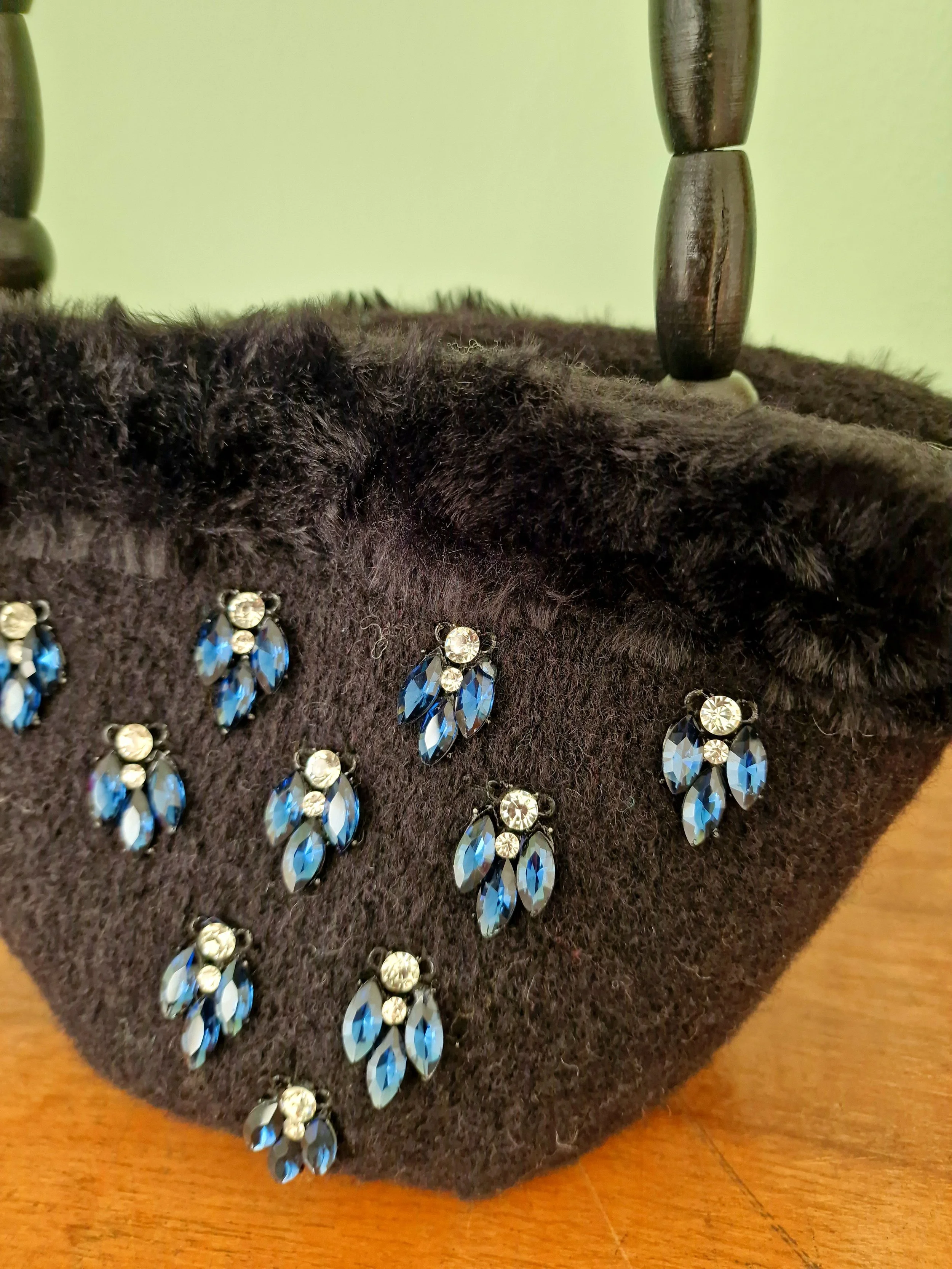 Dettaglio ricamo gioiello con cristalli blu su borsa in lana nera, rifinita in pelliccia. Accessorio artigianale siciliano di lusso.
