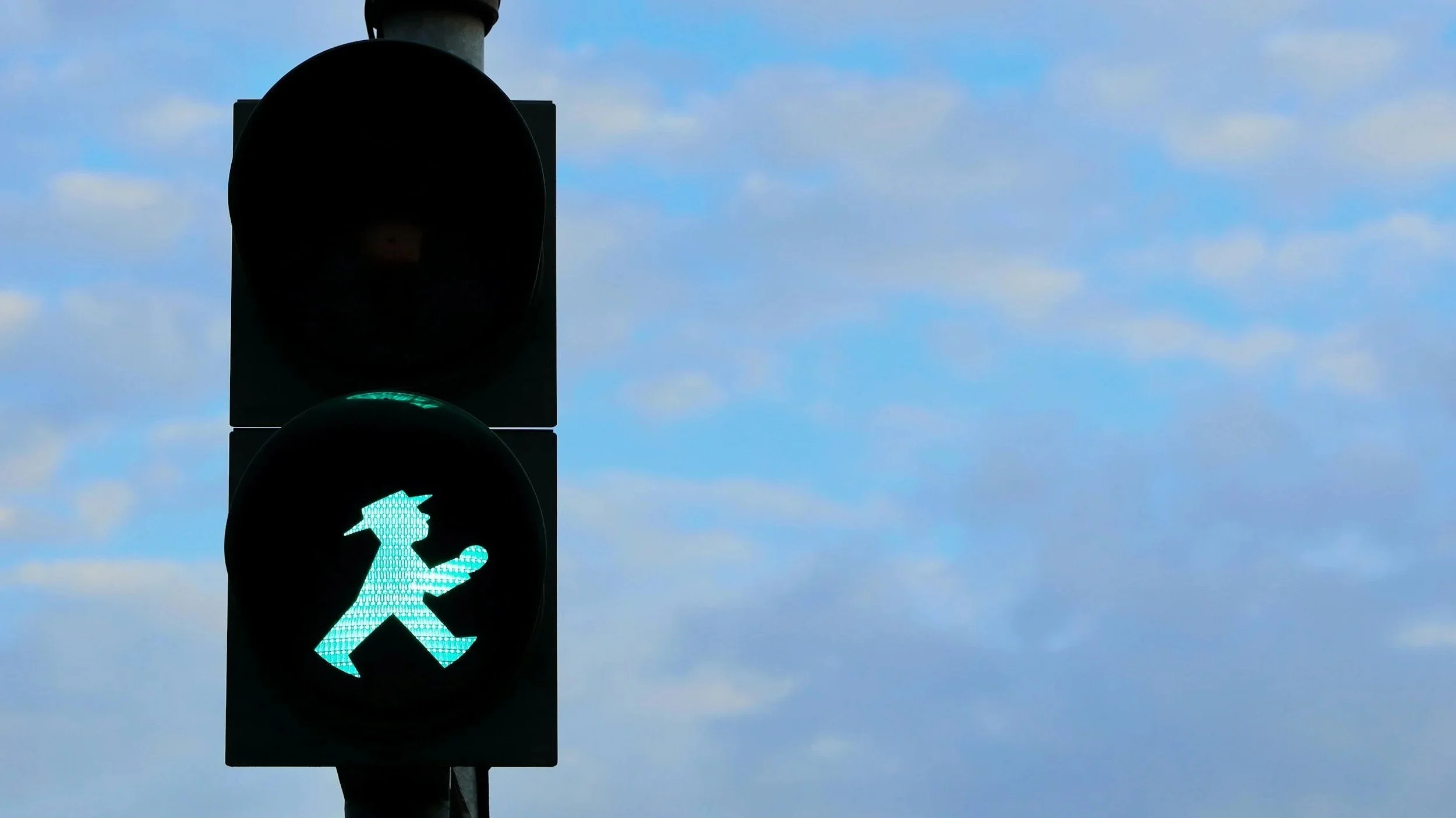 A traffic light shows a green pedestrian signal with a walking figure.