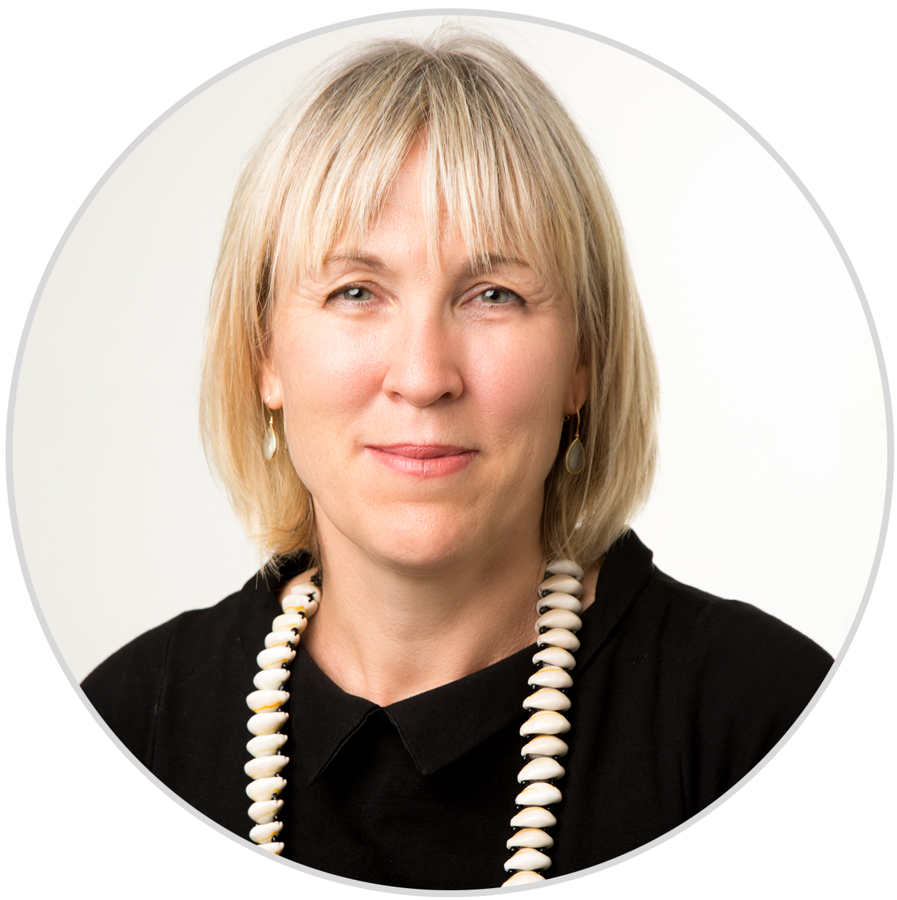 Portrait of a middle-aged woman with blonde hair, wearing a black top, shell necklace, and earrings, against a white background.